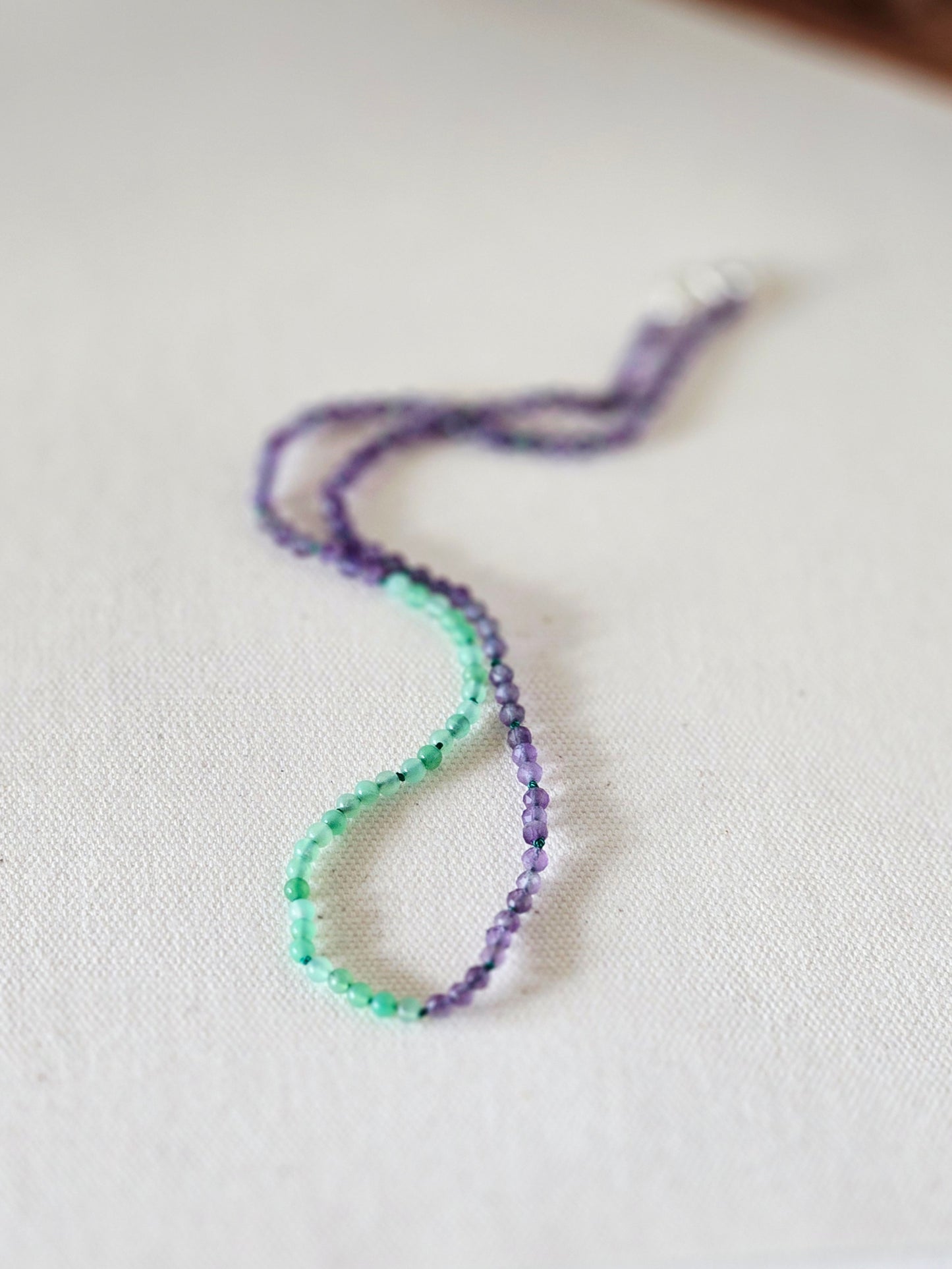 Beaded necklace with purple and green beads on a light fabric background