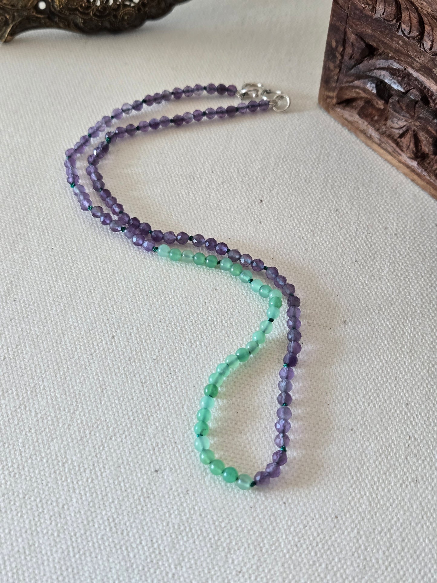 Beaded necklace with purple and green beads on a textured surface
