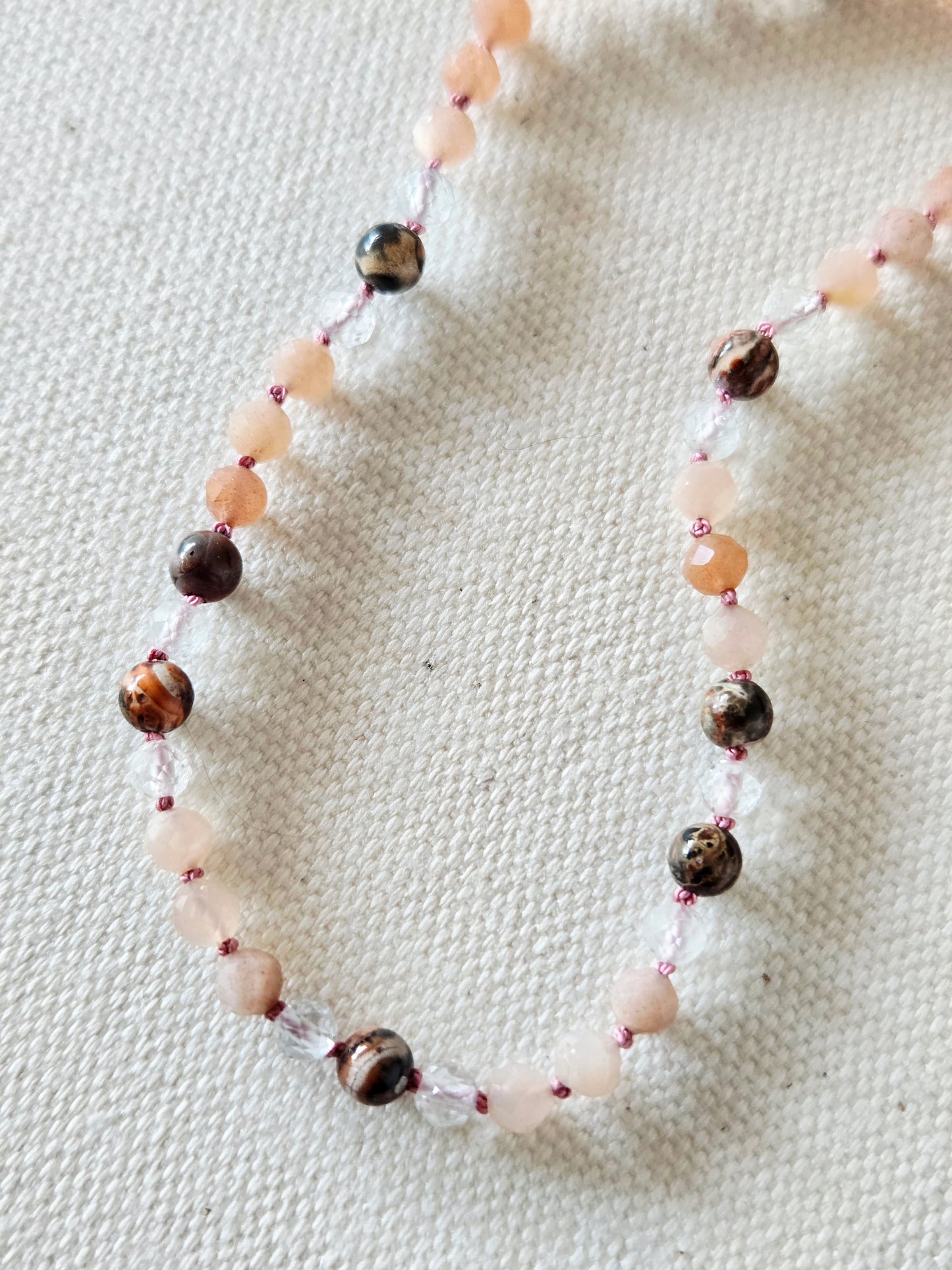 Necklace with peach, pink, and multicolored beads on a textured fabric background