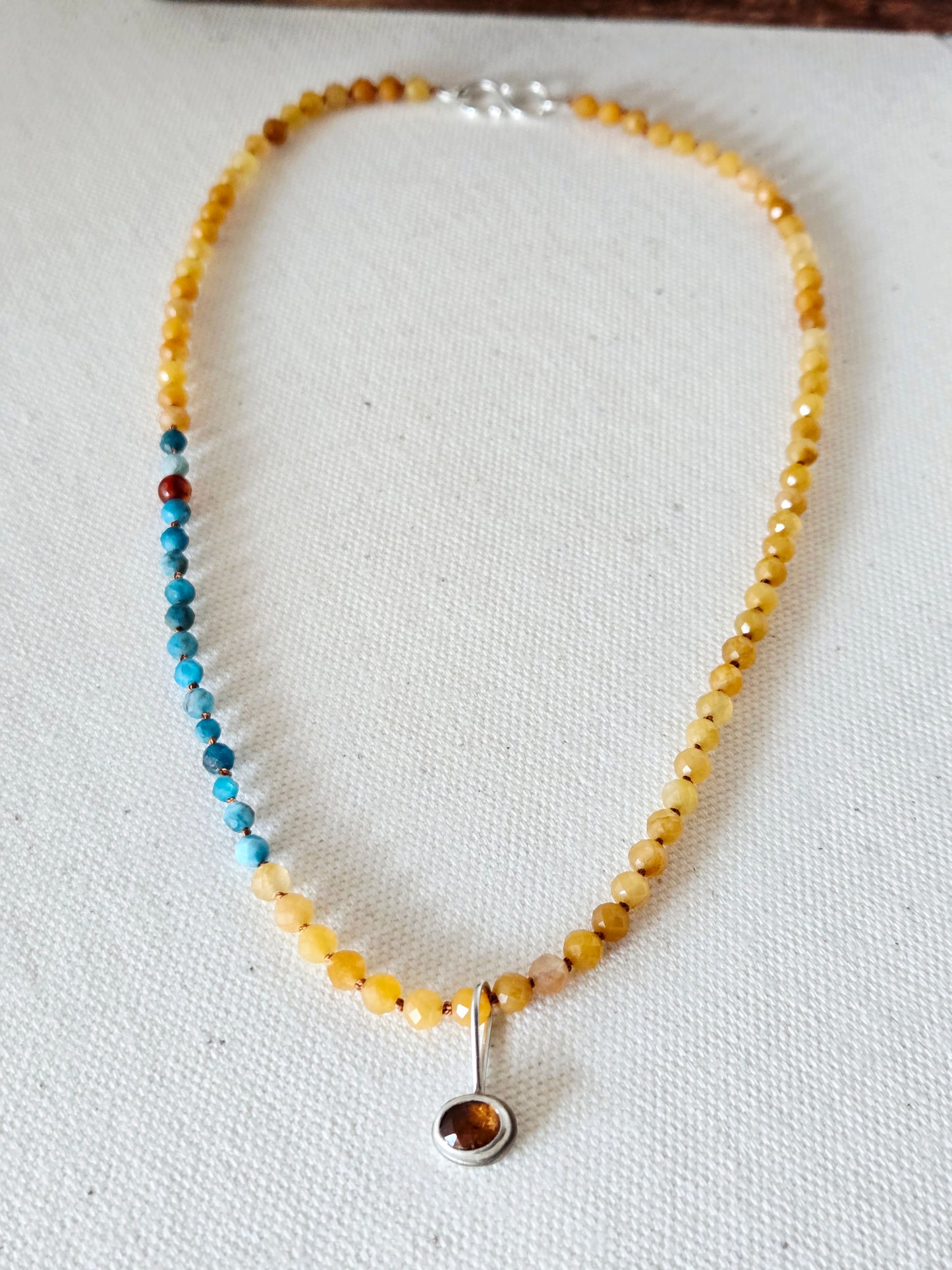 Necklace with yellow beads and a silver pendant on a white fabric background