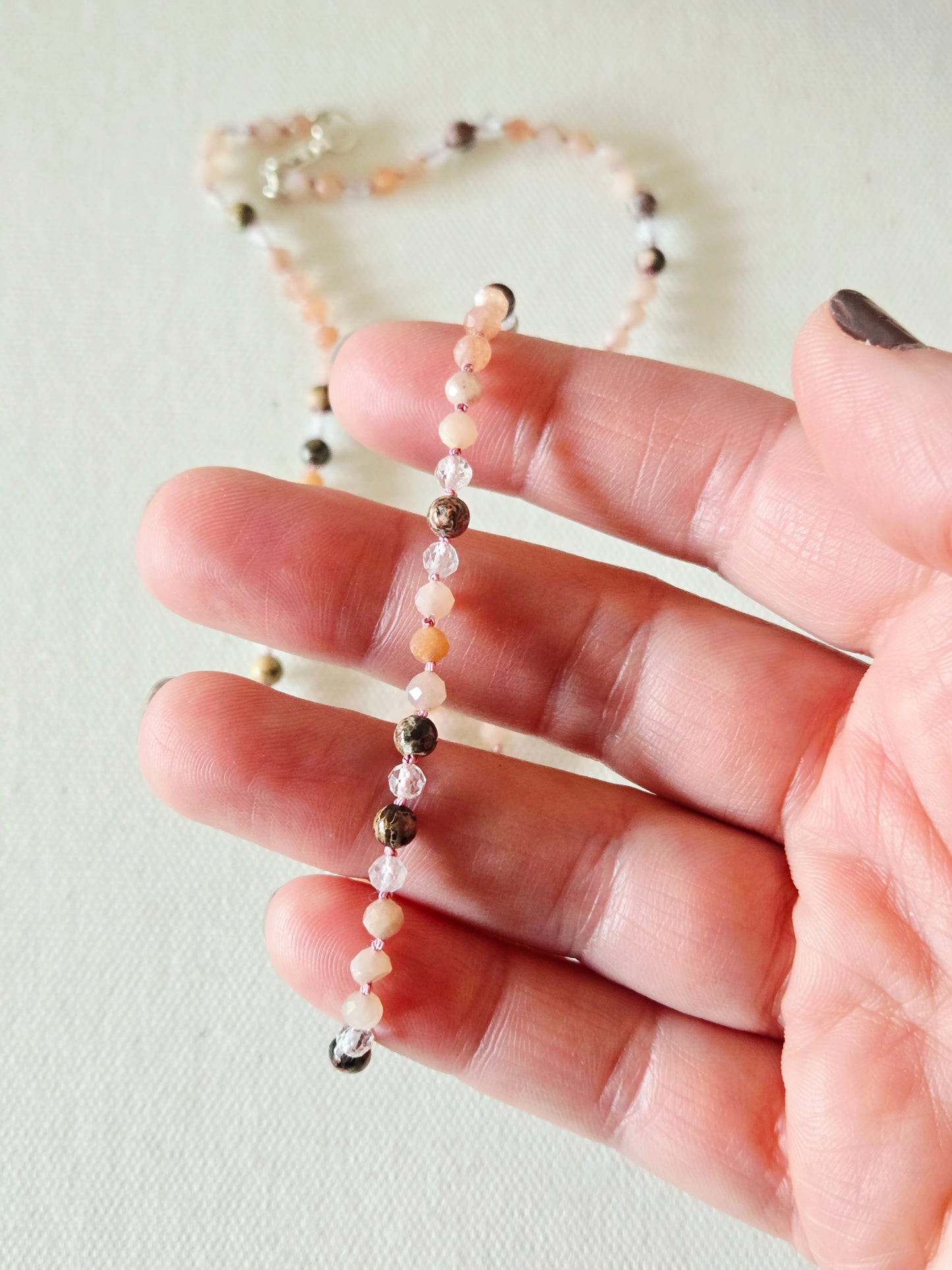 Beaded necklace held between fingers on a light background