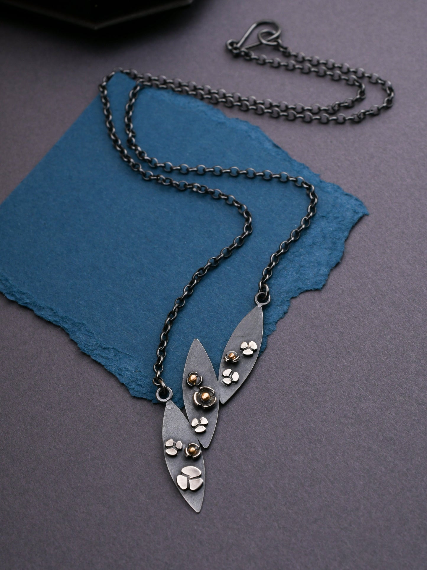 Black silver leaf and flower necklace on a dark gray and blue textured surface