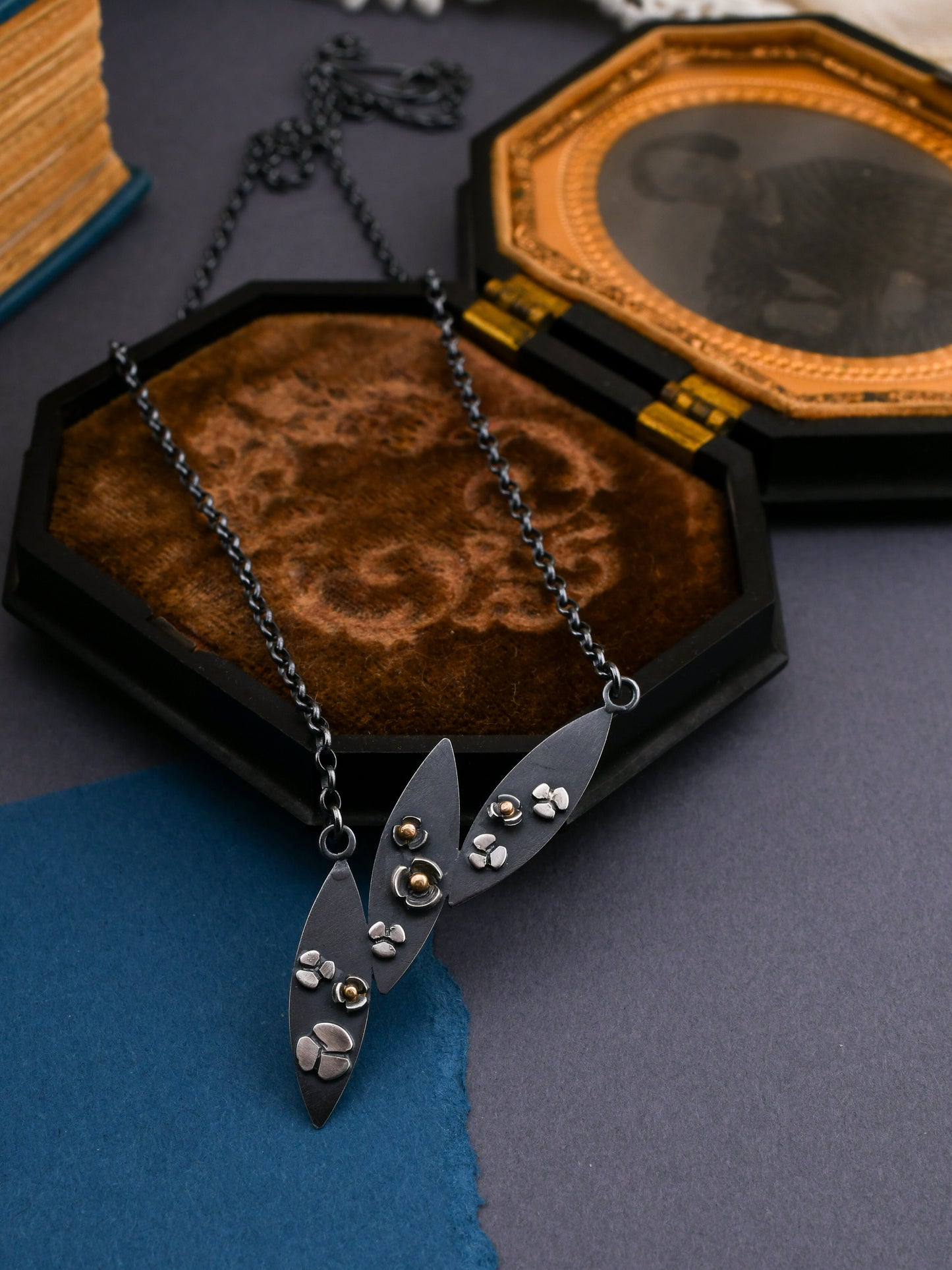 3 leaf necklace with flowers displayed on a brown velvet photo frame with a dark gray background