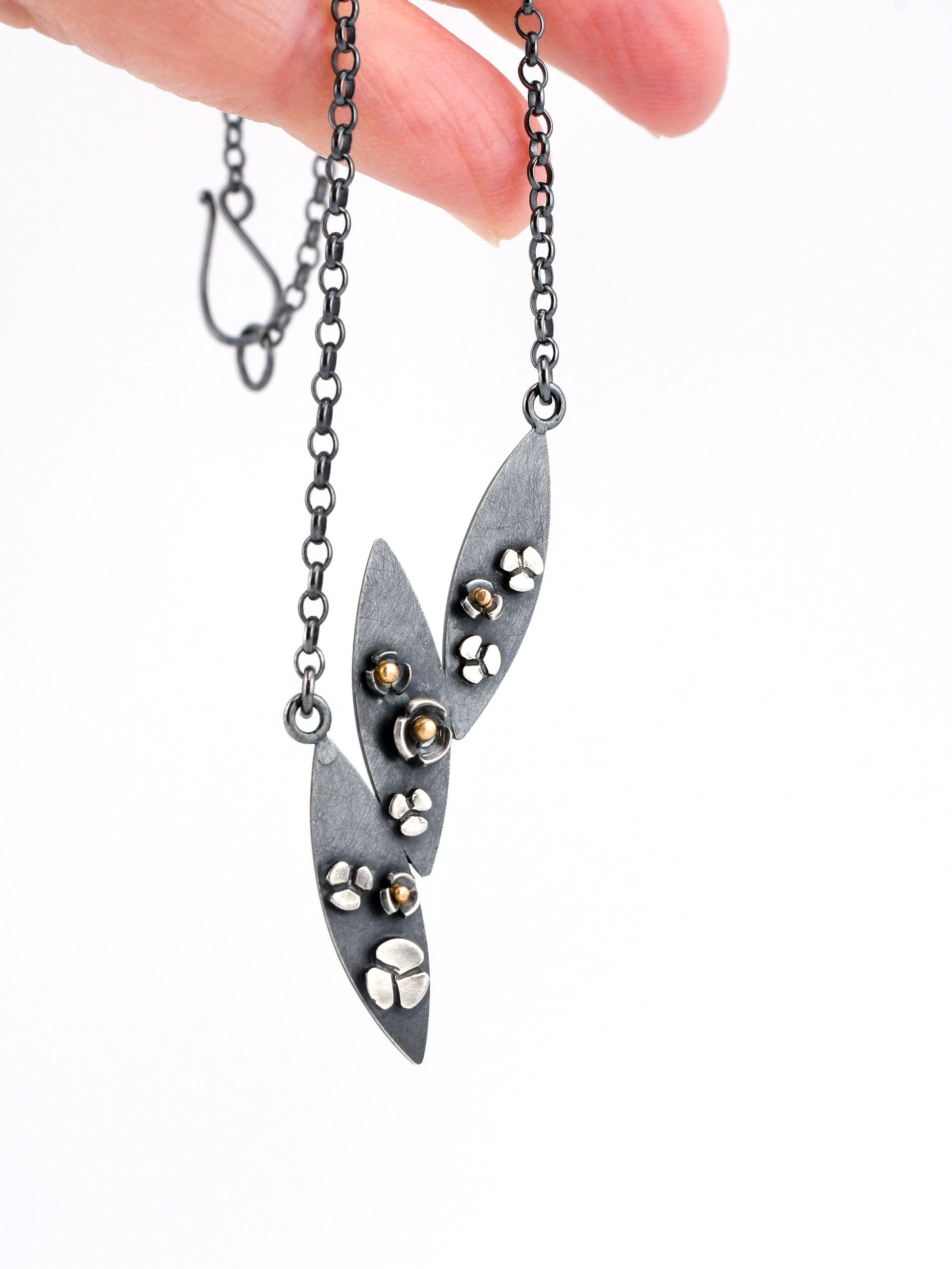 3 leaf black silver necklace with flowers and gold accents held by a hand on a white background