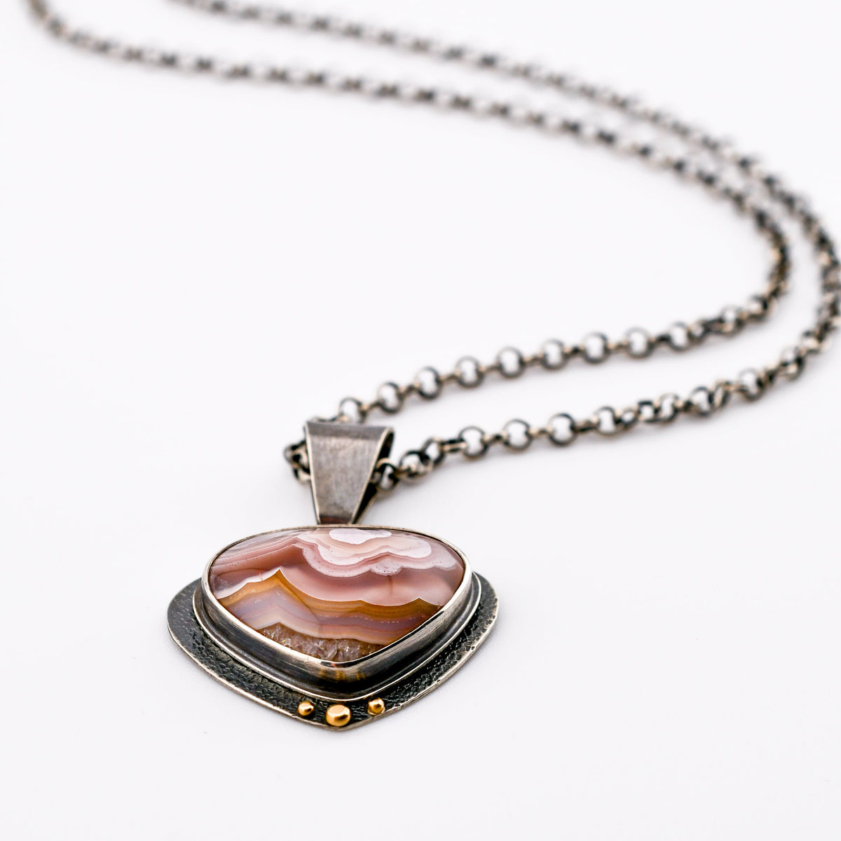 a rounded agua nueva agate in shades of pink, rose and gold has a textured backplate that swings behind the stone and is accented with 14k gold