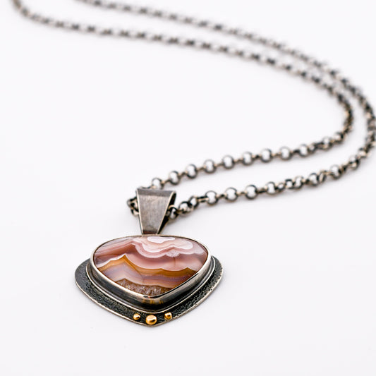 a rounded agua nueva agate in shades of pink, rose and gold has a textured backplate that swings behind the stone and is accented with 14k gold