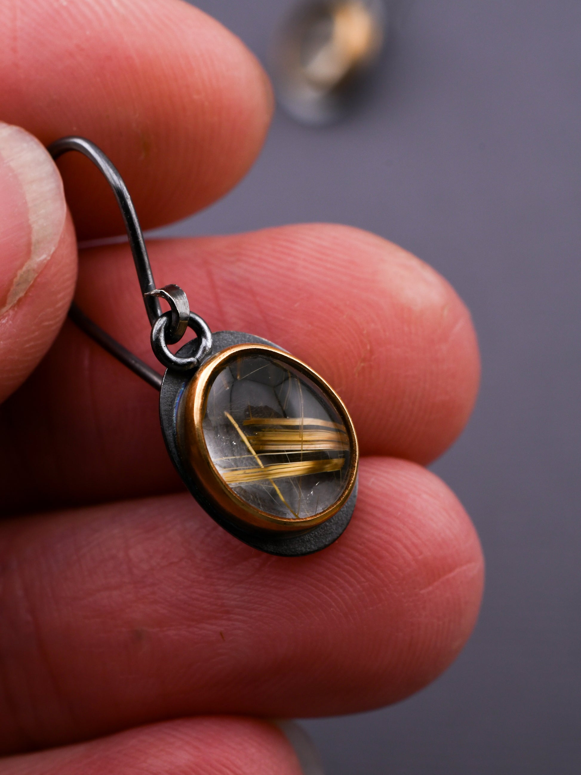 Close-up of a hand holding a silver and gold earring with a gemstone