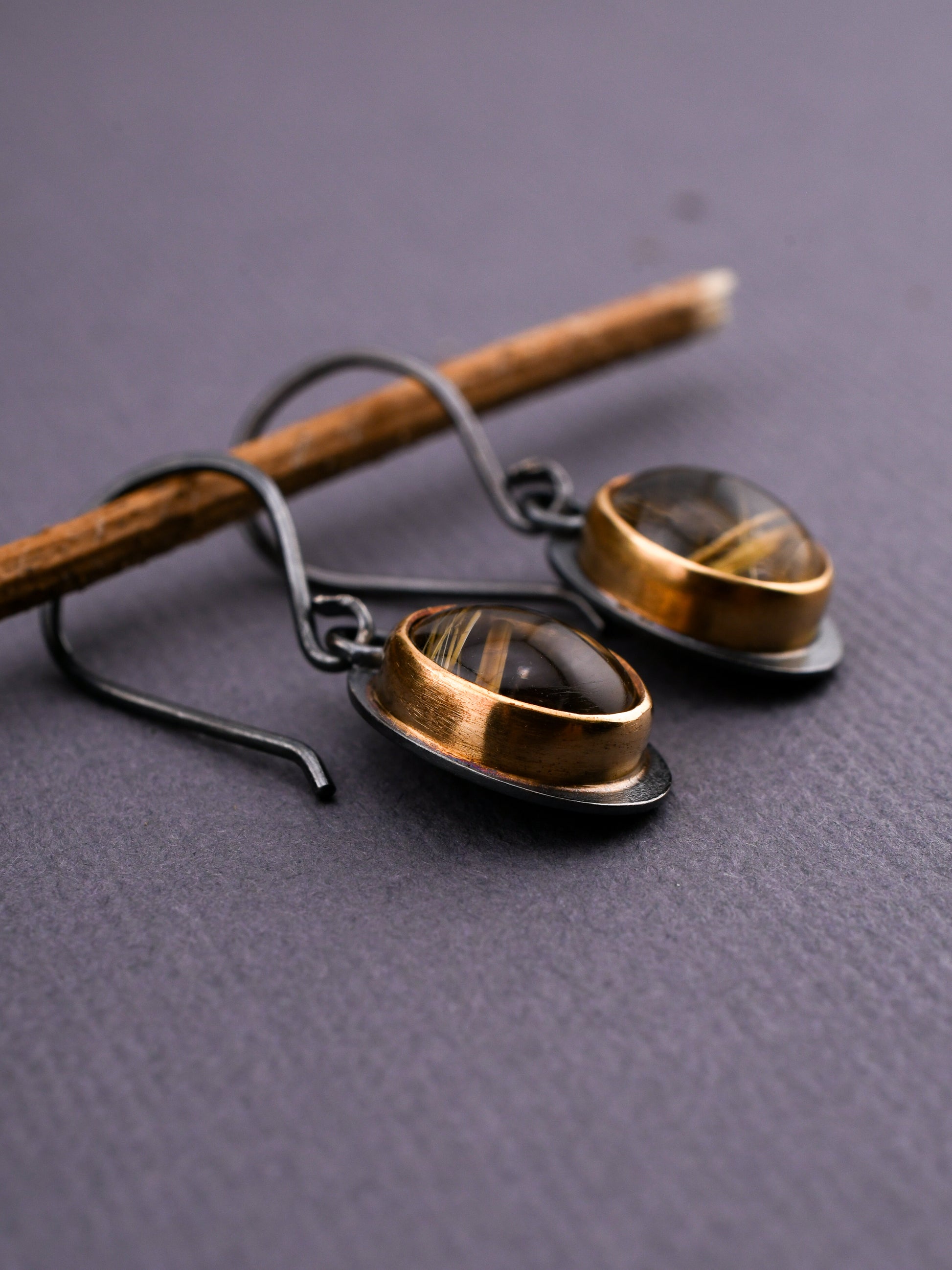 Pair of gold and black earrings on a textured gray surface