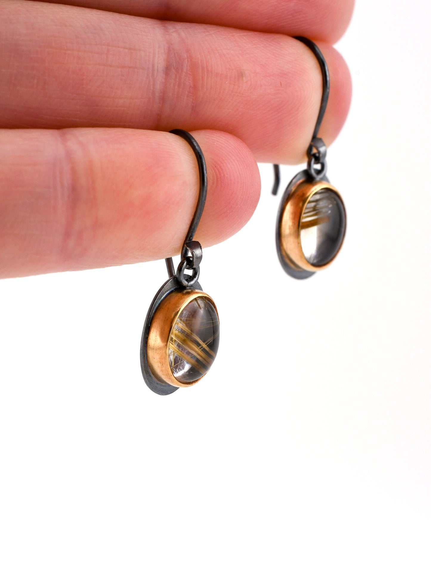 Pair of earrings with oval designs held between fingers on a white background