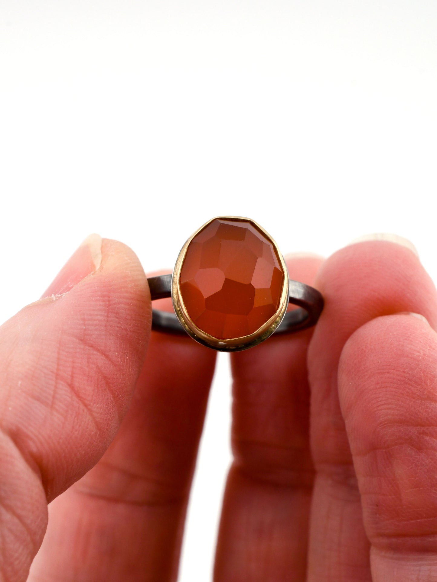 Ring with a large red-colored stone held between fingers against a white background