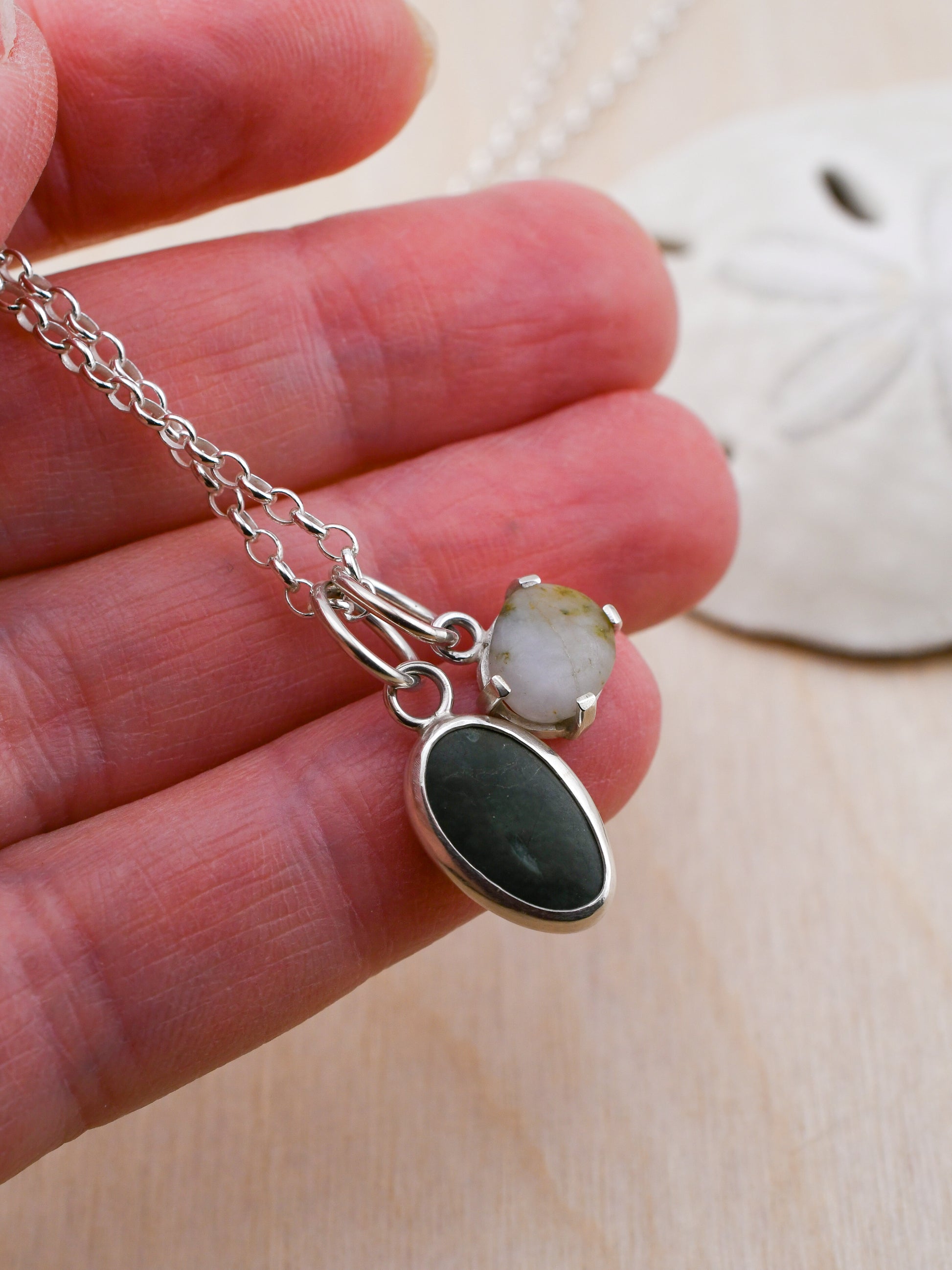 Necklace with two beach stone charms held between fingers on a light wooden surface