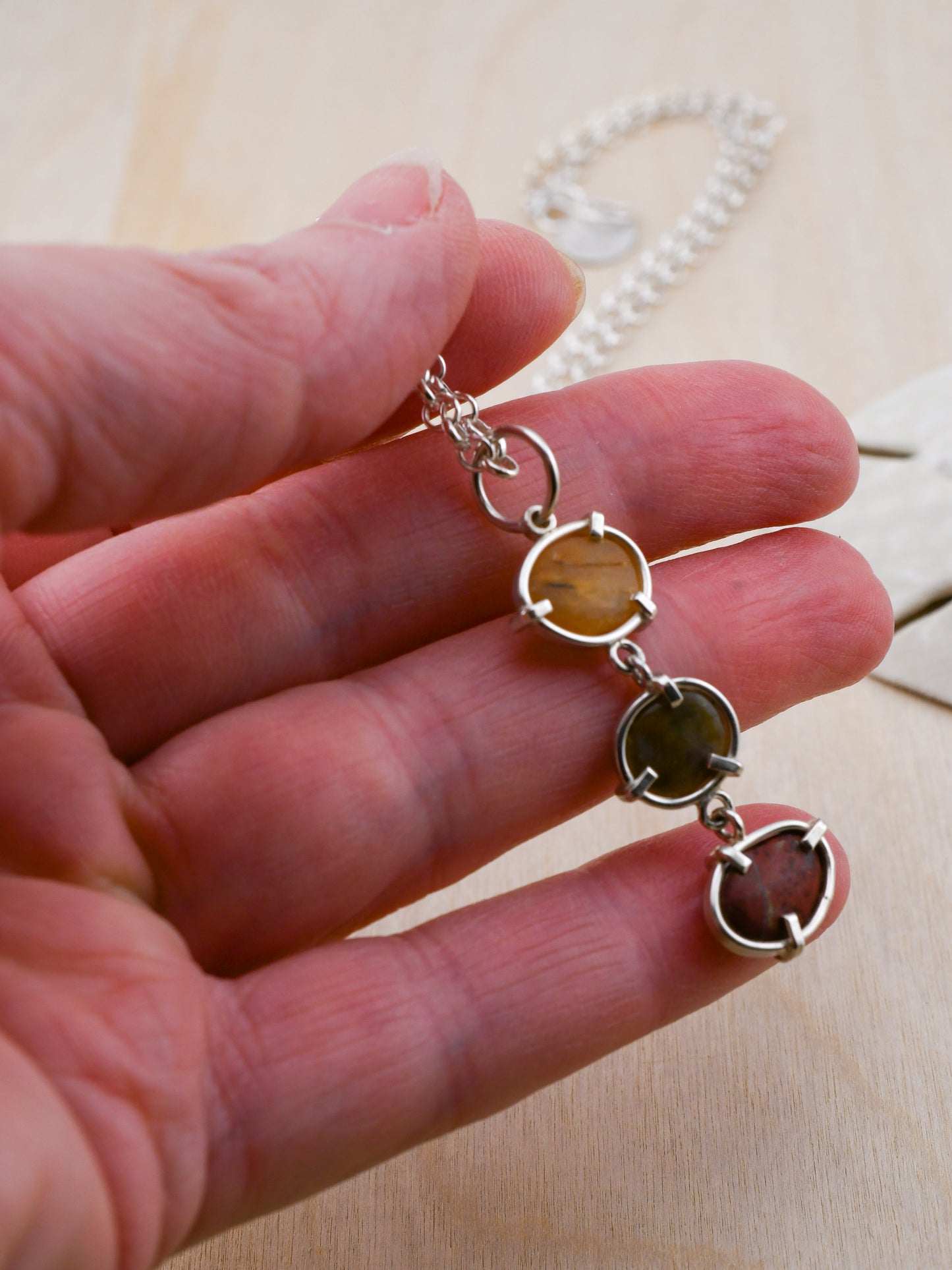 Silver pendant with 3 beach stones held in a hand on a pale wood background