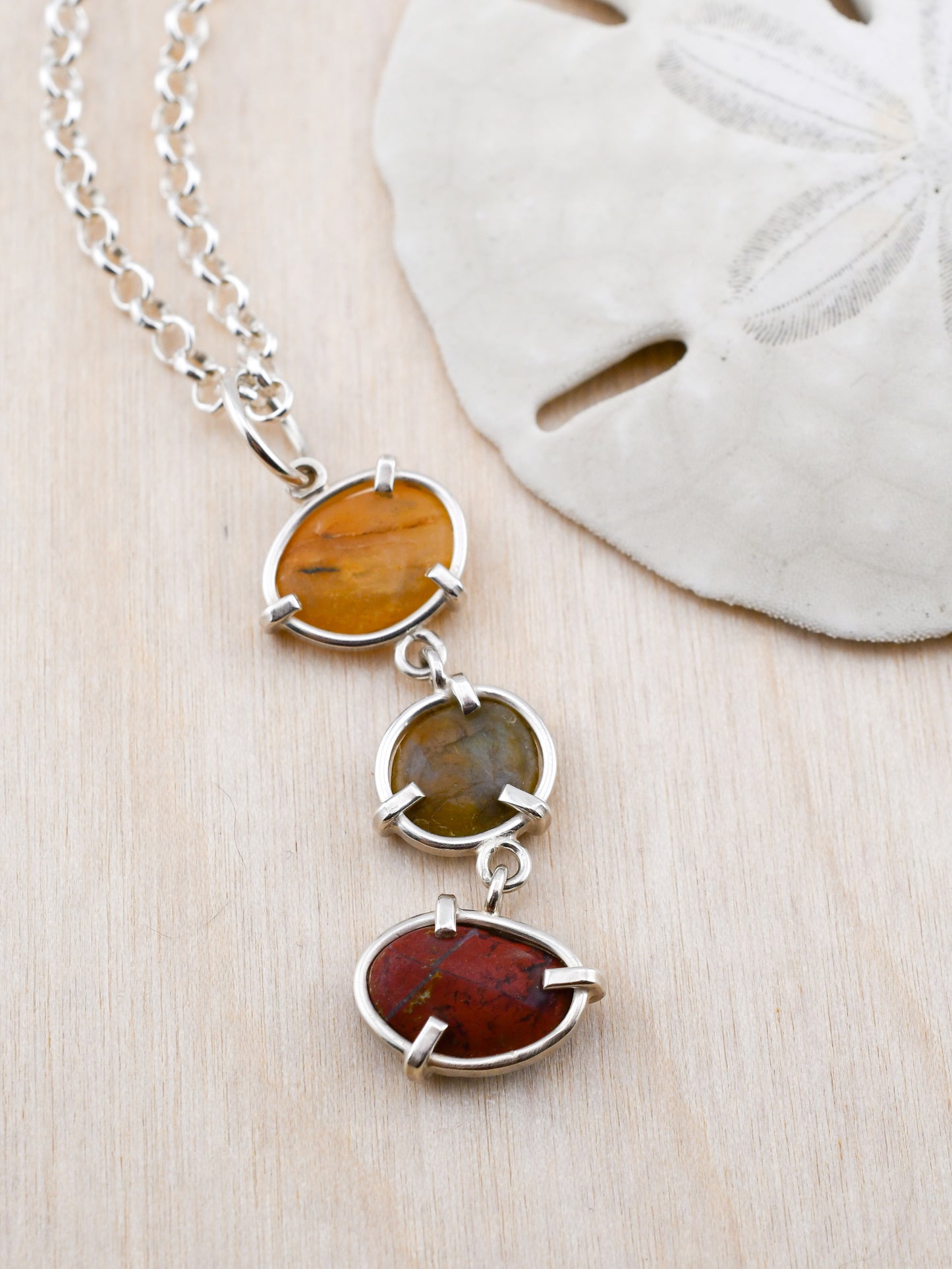 Necklace with three oval stones on a wooden surface next to a sand dollar.