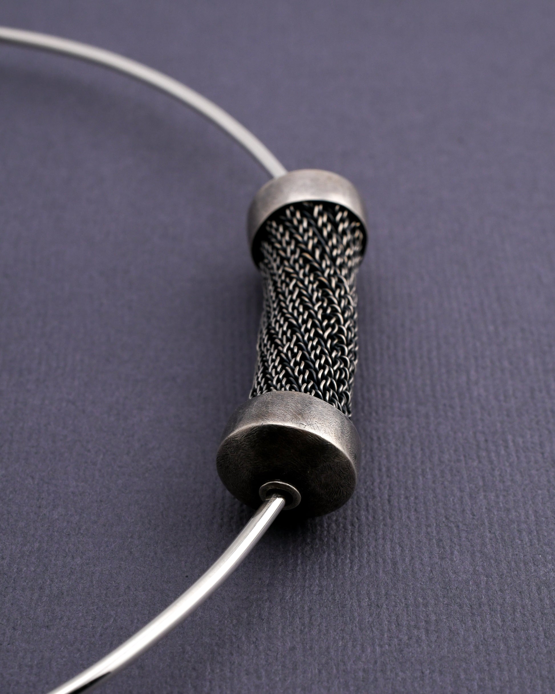 closeup of woven bead element on a silver torque neckpiece on a textured gray background