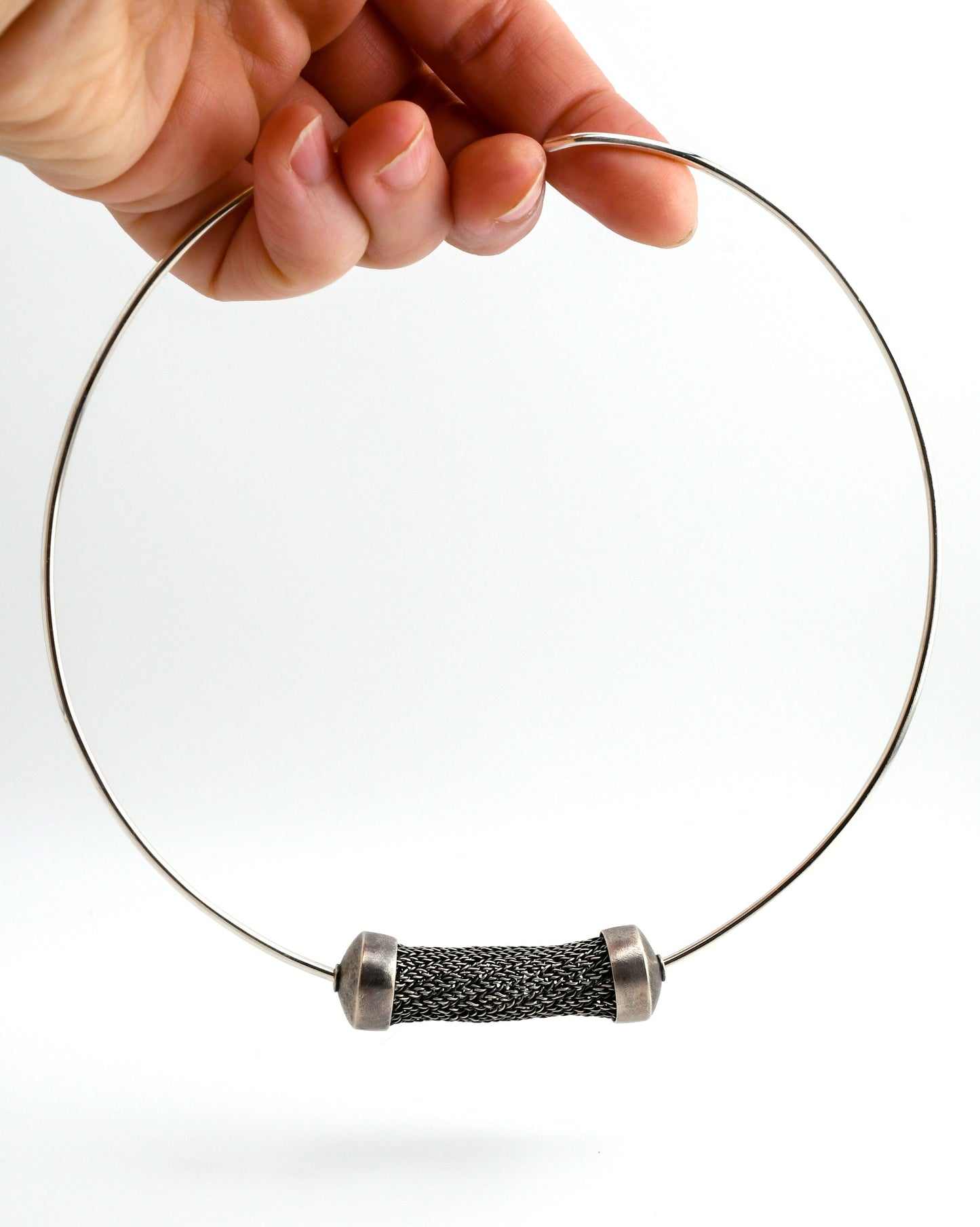 silver torque necklace with large sculptural woven bead suspended from a hand on a white background