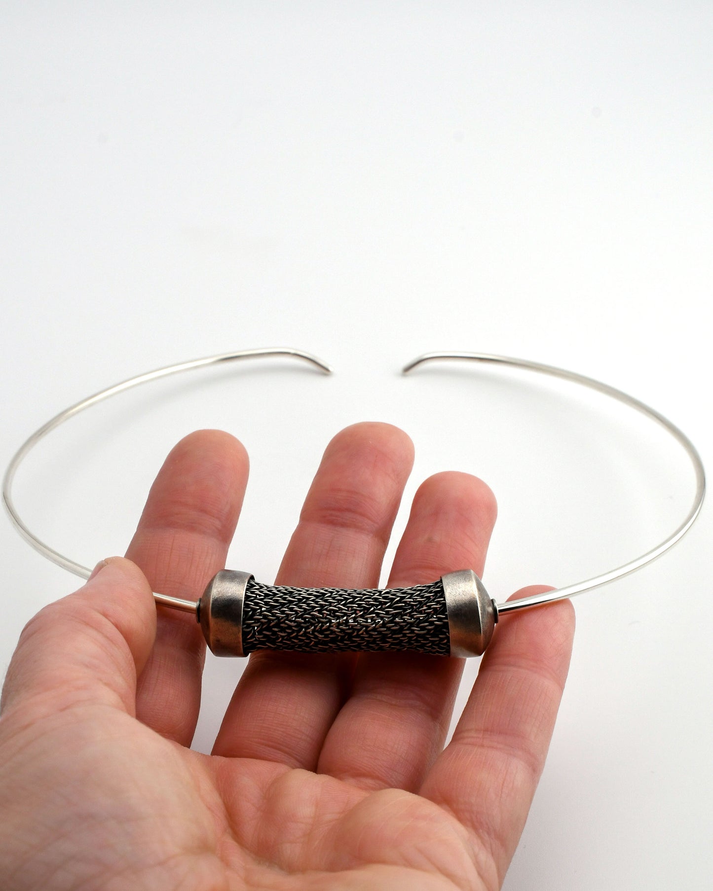 hand holding a woven bead on a silver torque over a white background