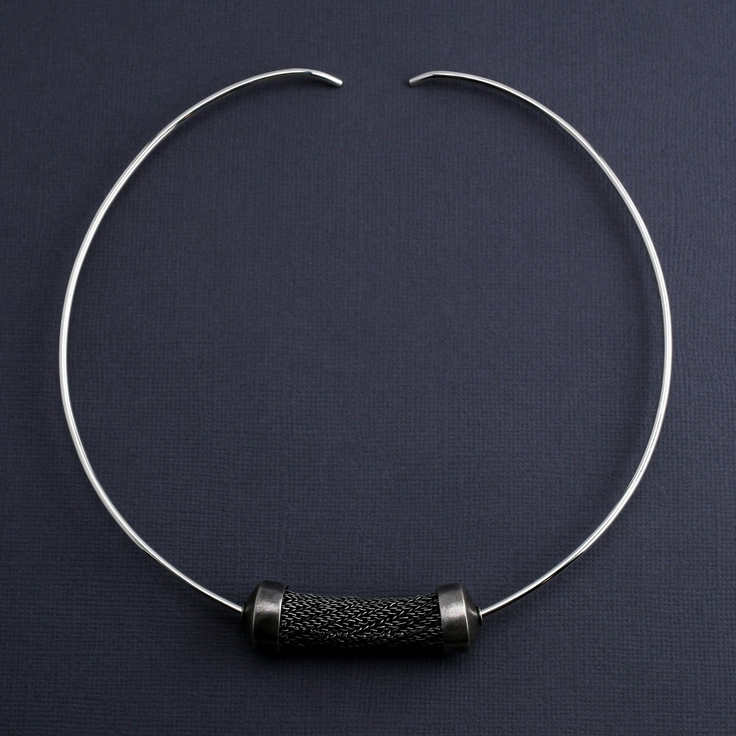 Silver torque necklace with large sculptural woven bead on a dark gray background