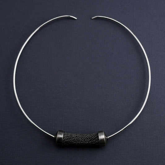 Silver torque necklace with large sculptural woven bead on a dark gray background