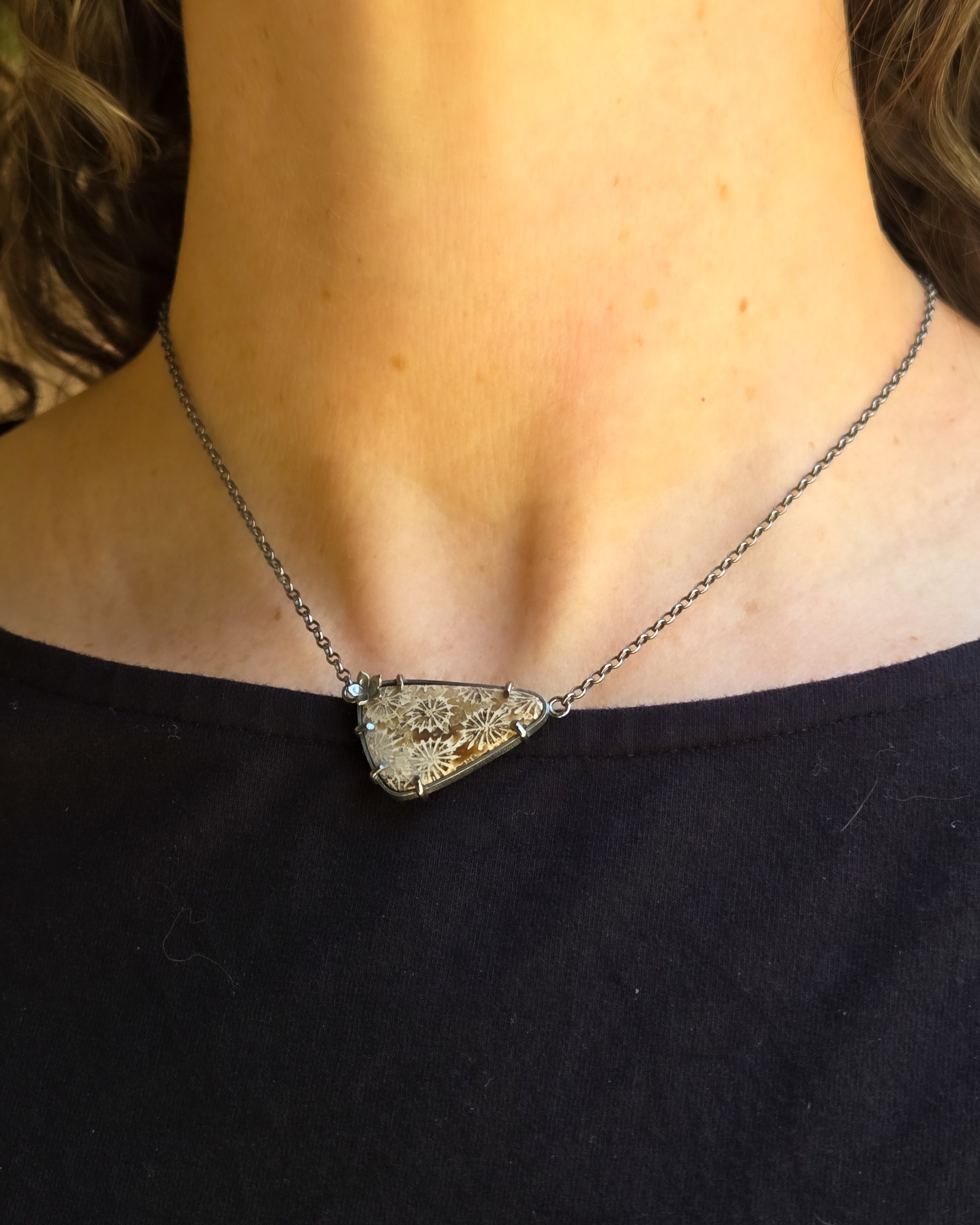 Necklace with a triangular pendant worn by a person wearing a black top