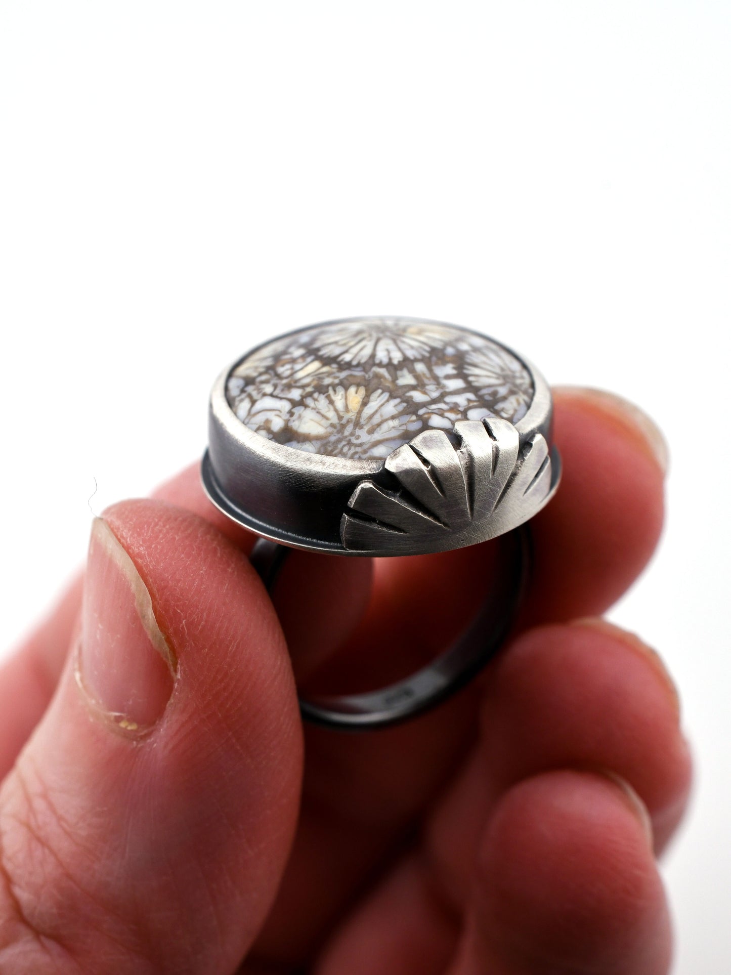 Silver ring with floral design held in a hand against a white background
