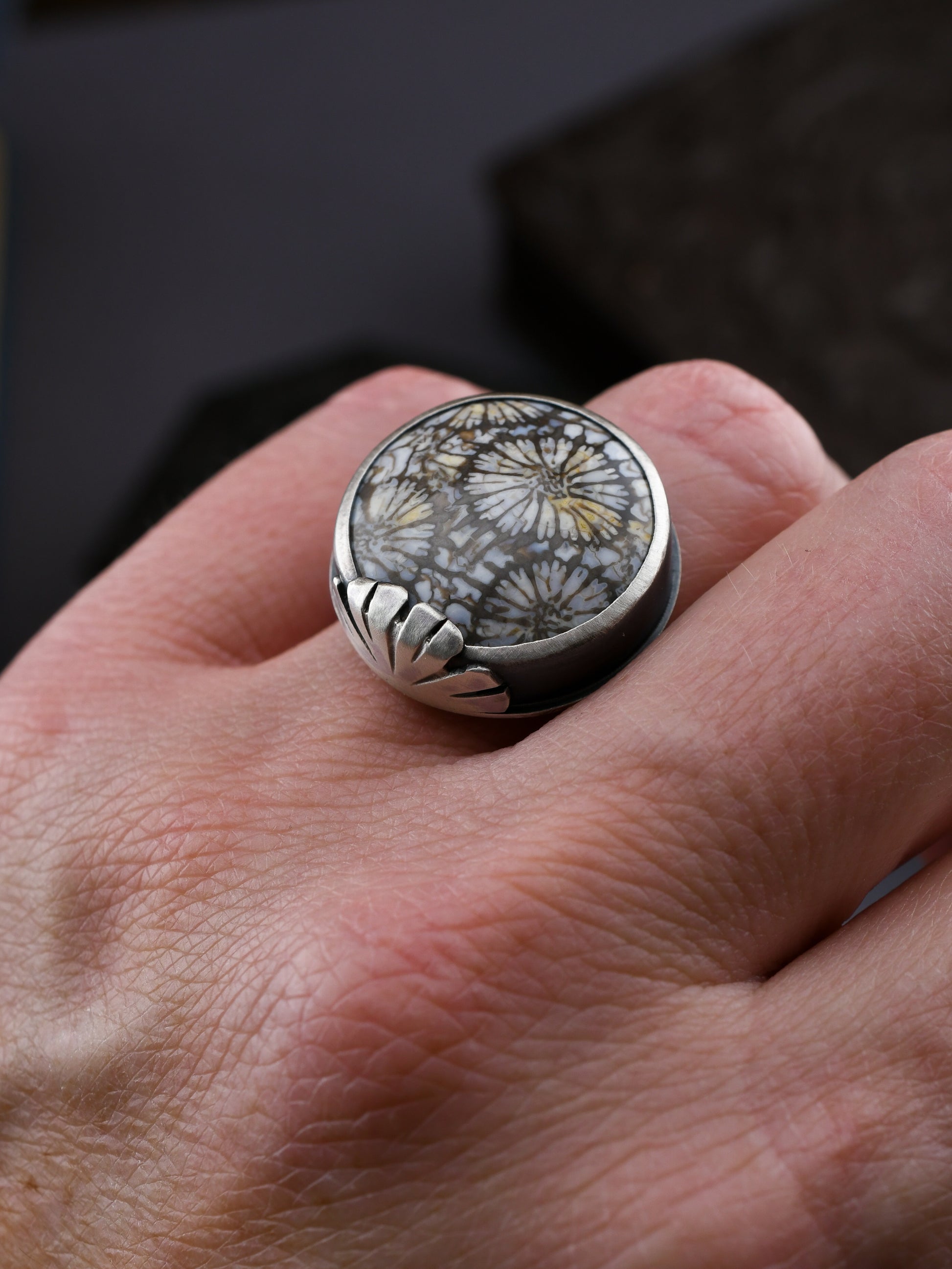 Silver ring with a natural stone on a hand against a dark background