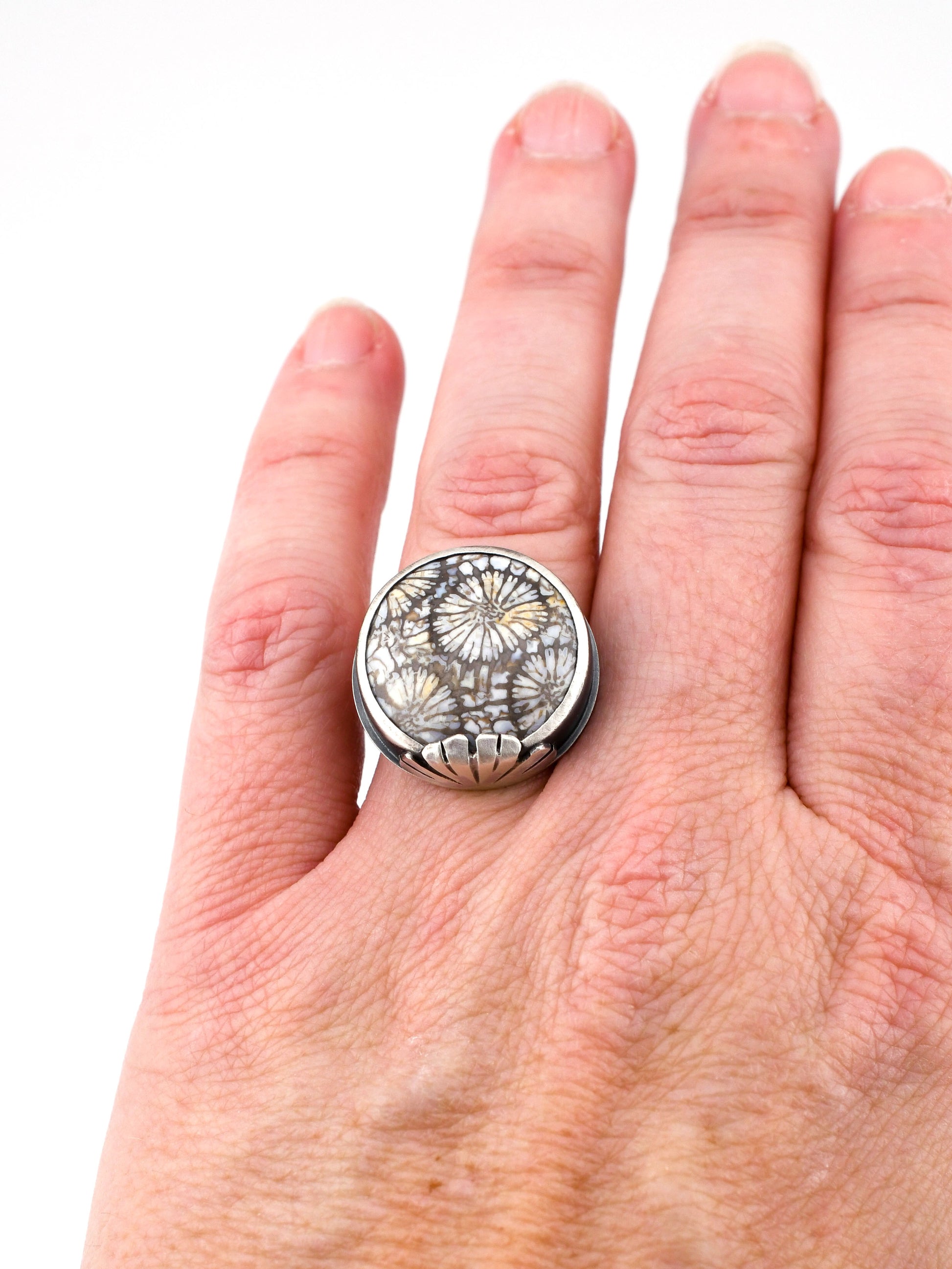 Silver ring with floral design on a hand against a white background