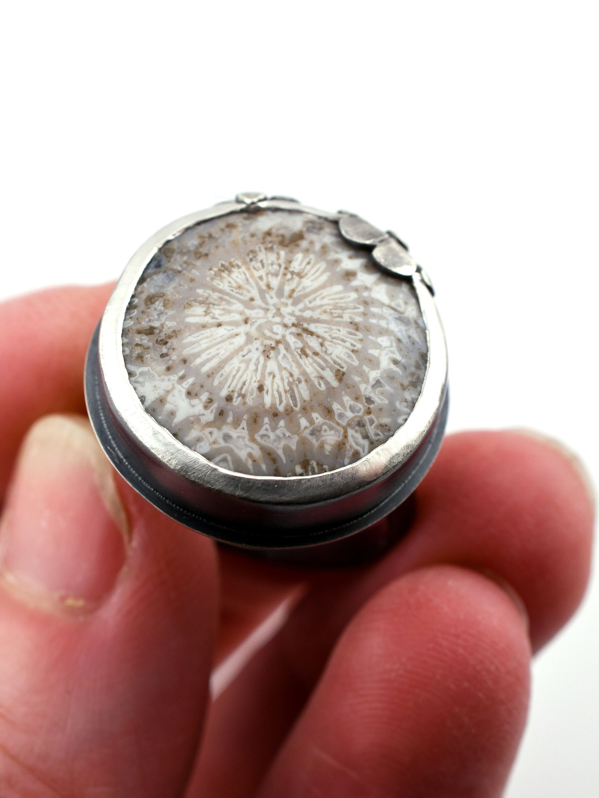 Close-up of a silver ring with a textured stone held between fingers against a white background