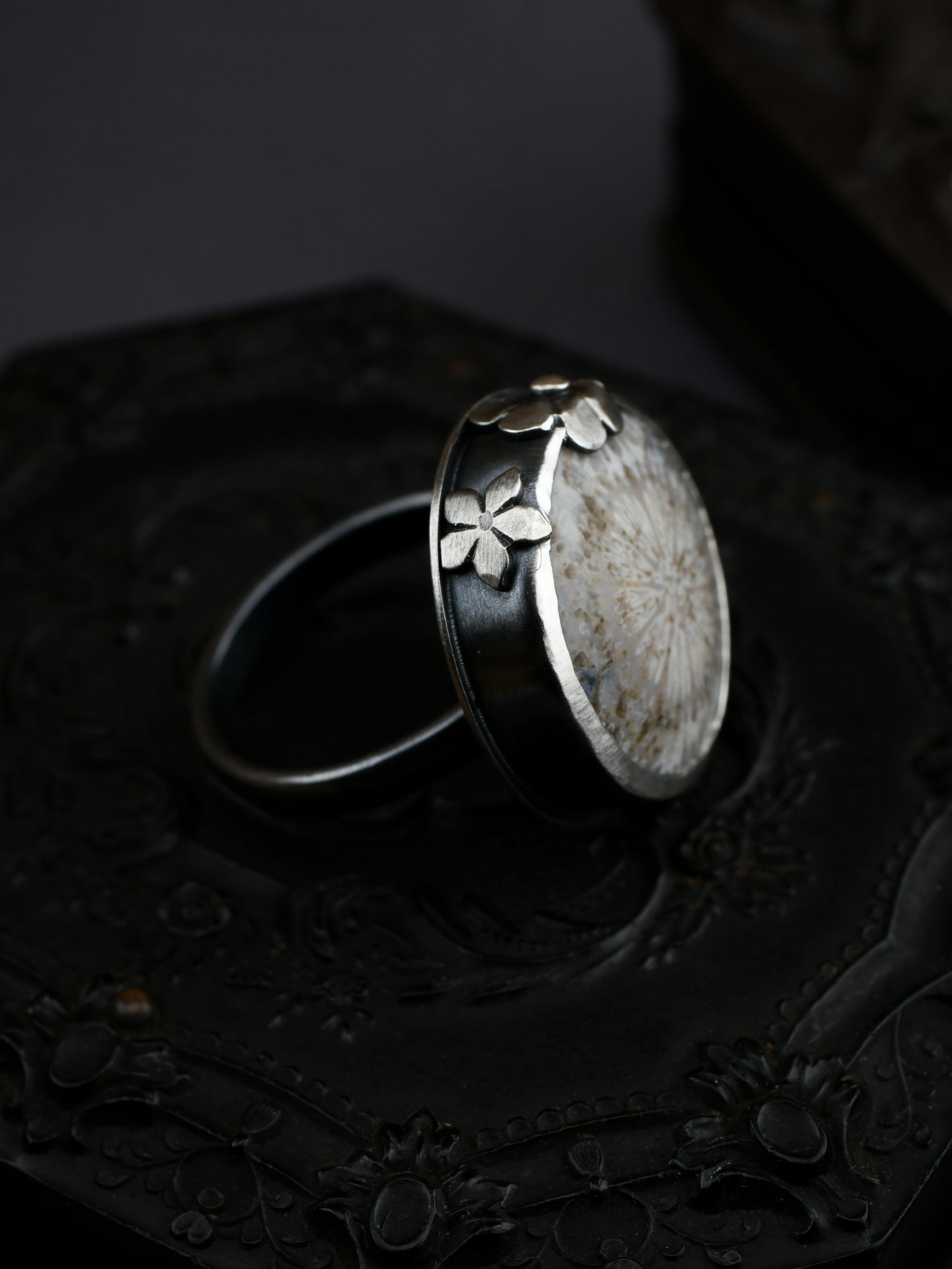 Silver ring with floral design on a dark textured surface