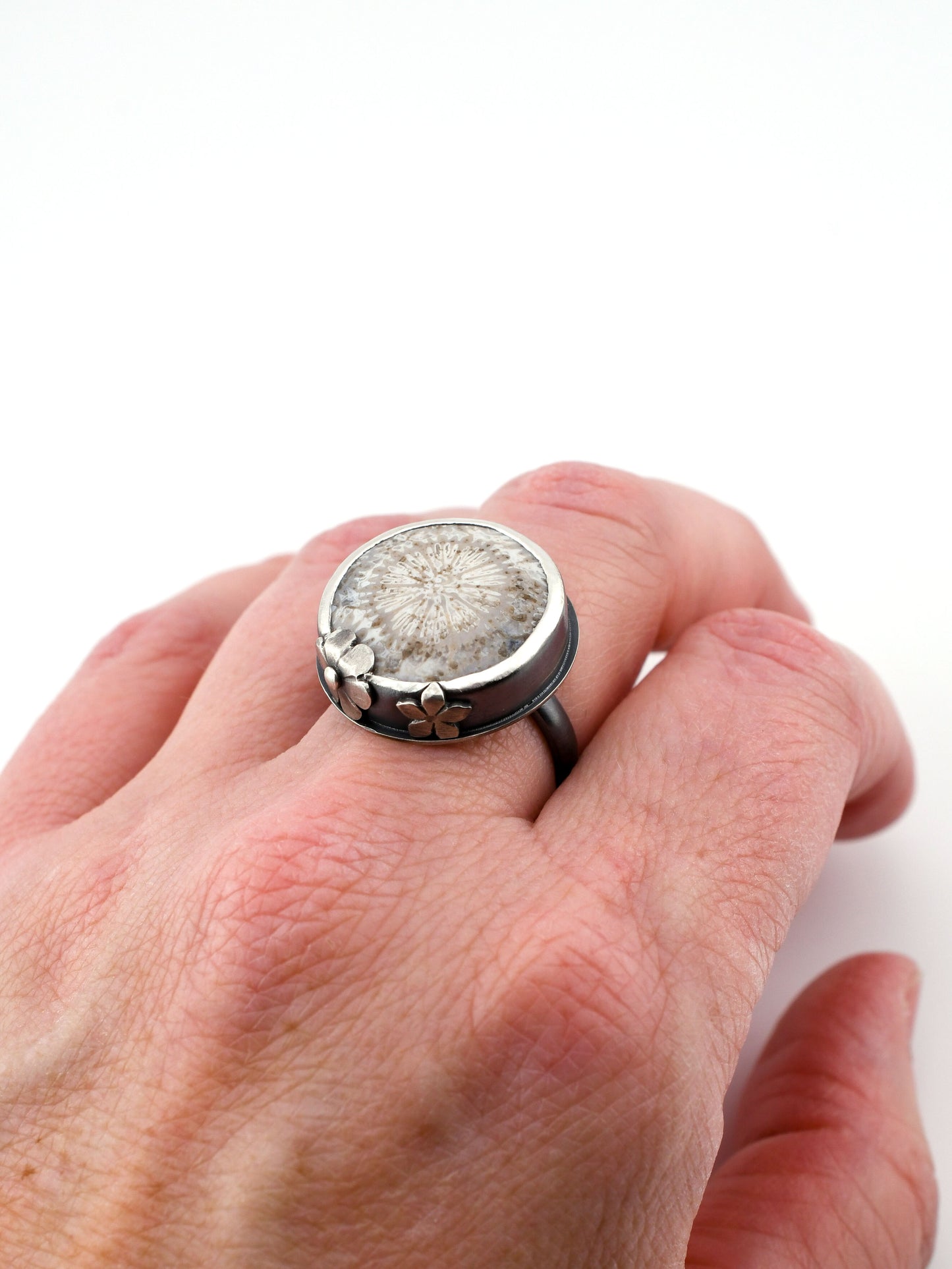 Hand wearing a ring with a textured stone and silver band on a white background