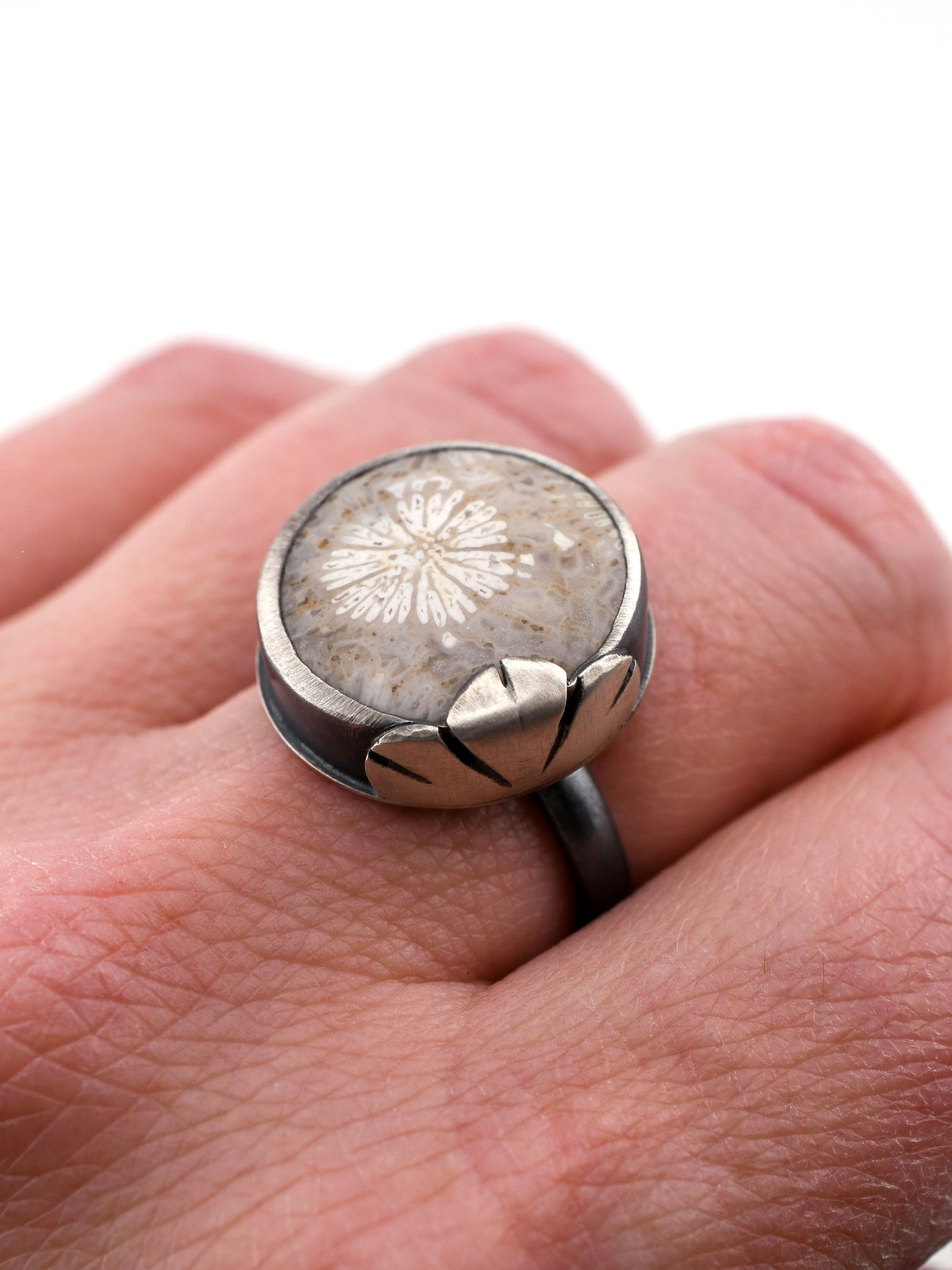 Silver ring with a fossilized coral stone on a hand against a white background