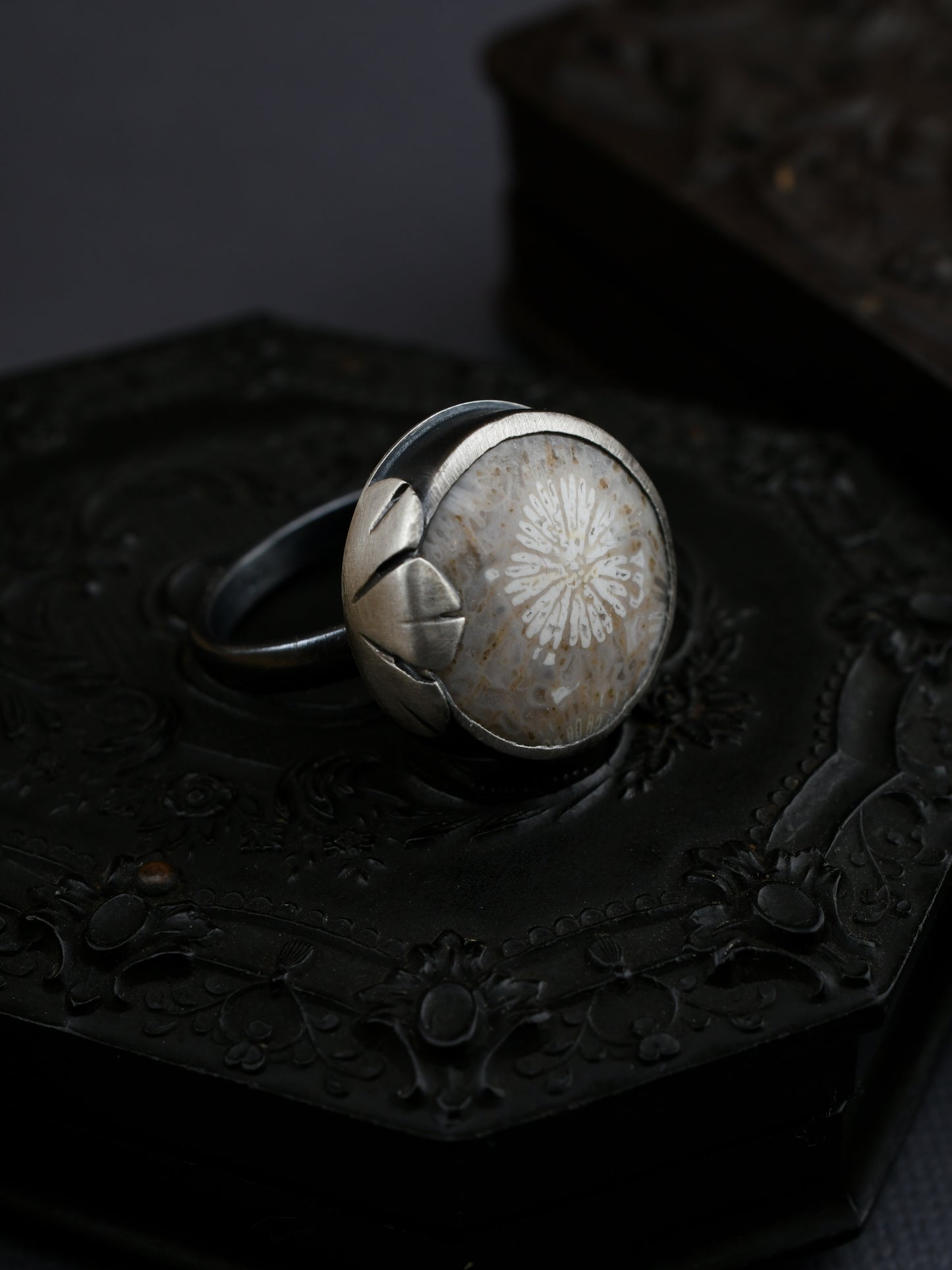 Silver ring with a floral design on a dark background