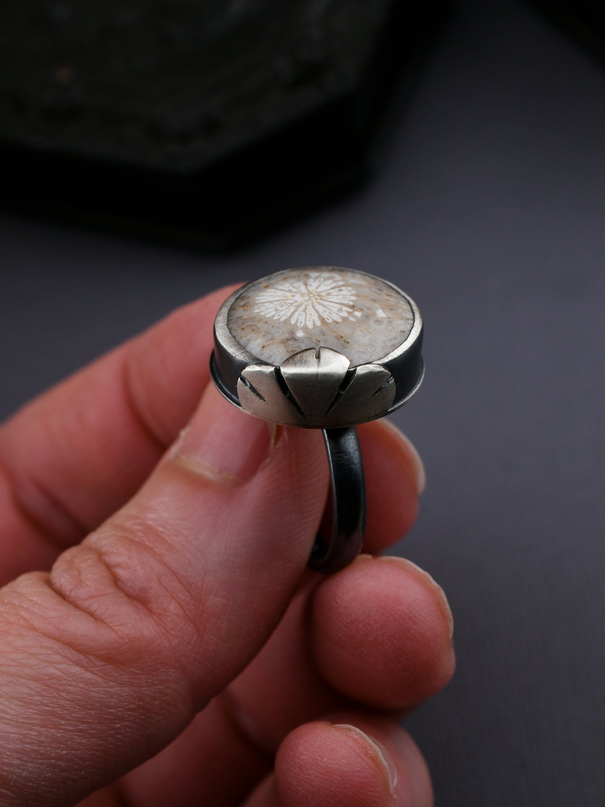 Silver ring with a floral design held in a hand against a dark background