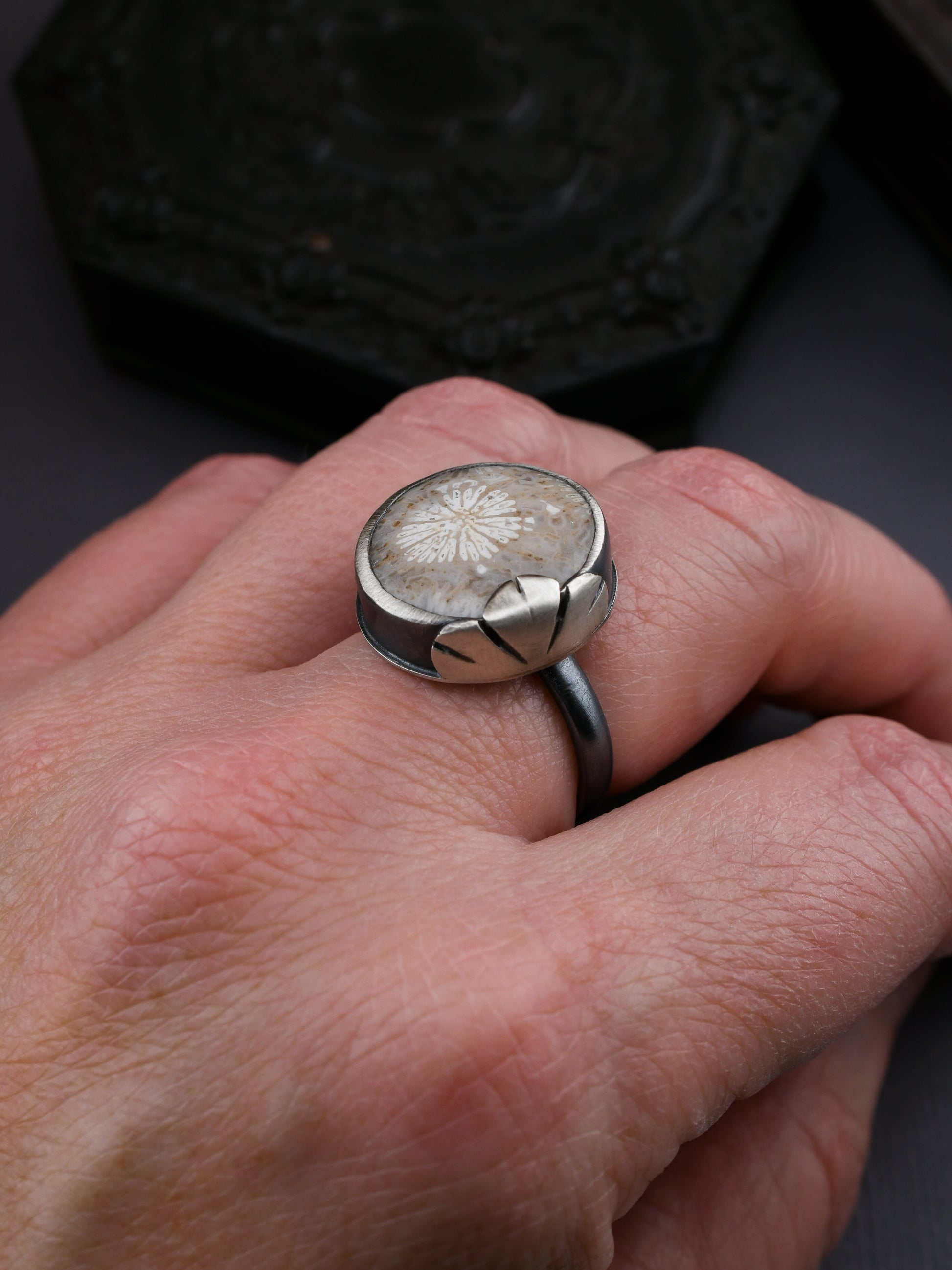Silver ring with a textured design on a person's finger against a dark background