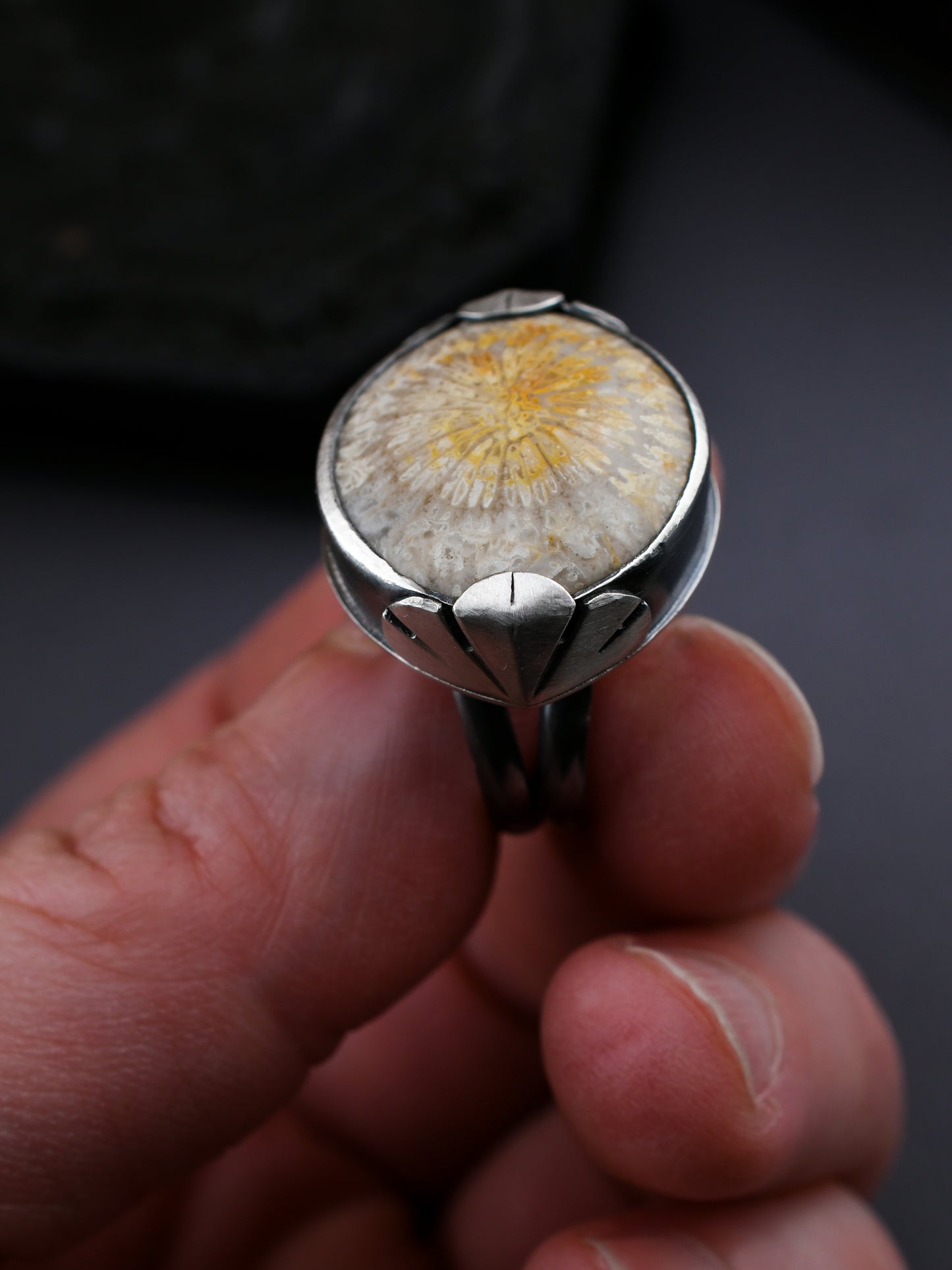 Silver ring with a floral design held in a hand against a dark background
