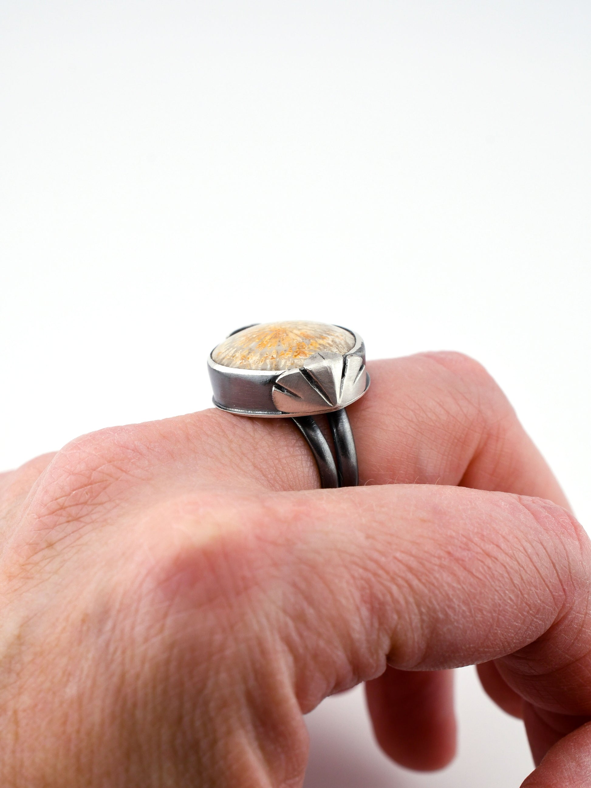 Silver ring with a fossilized coral stone on a hand against a white background