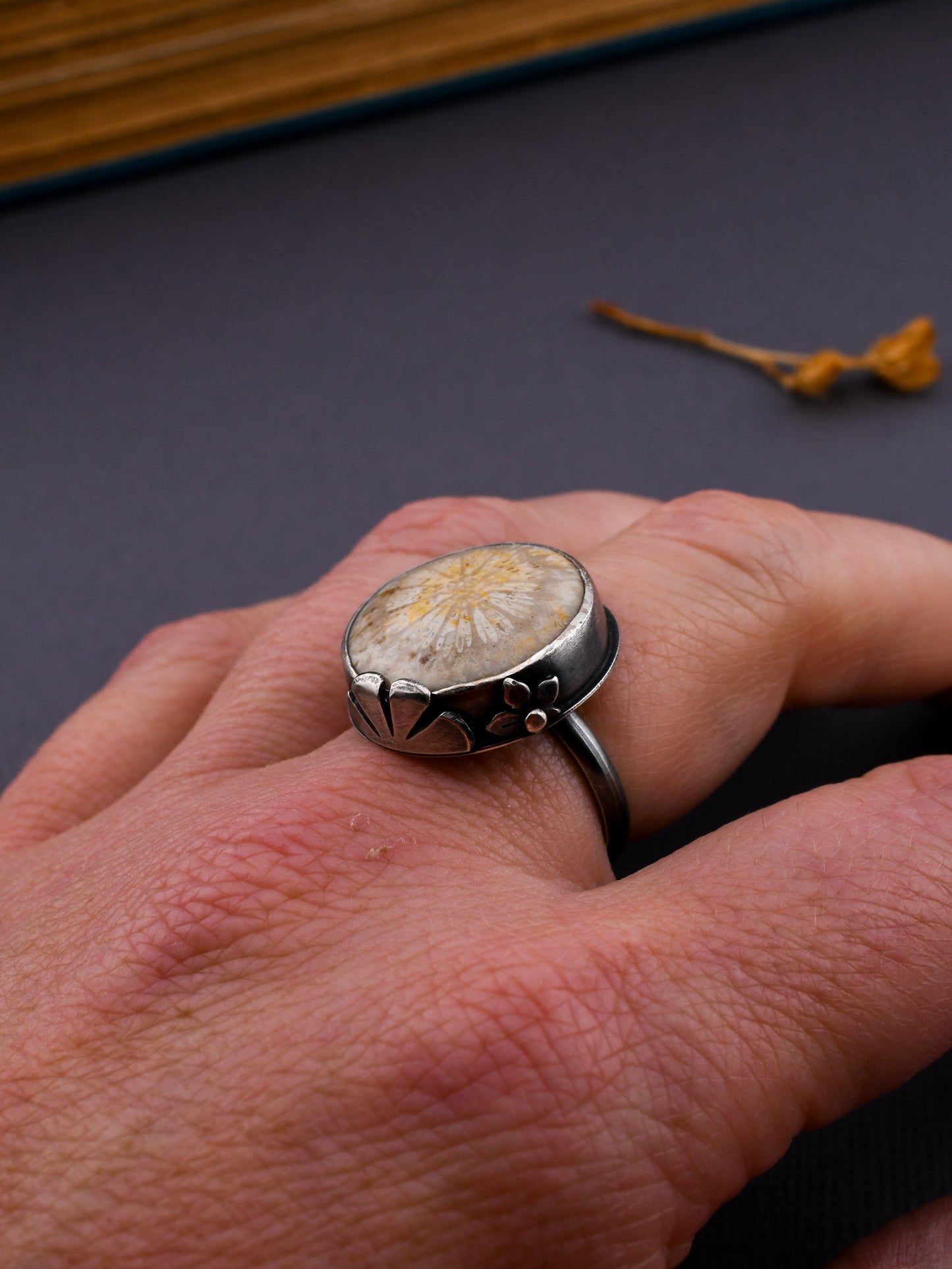 Silver ring with a floral design on a hand against a dark background