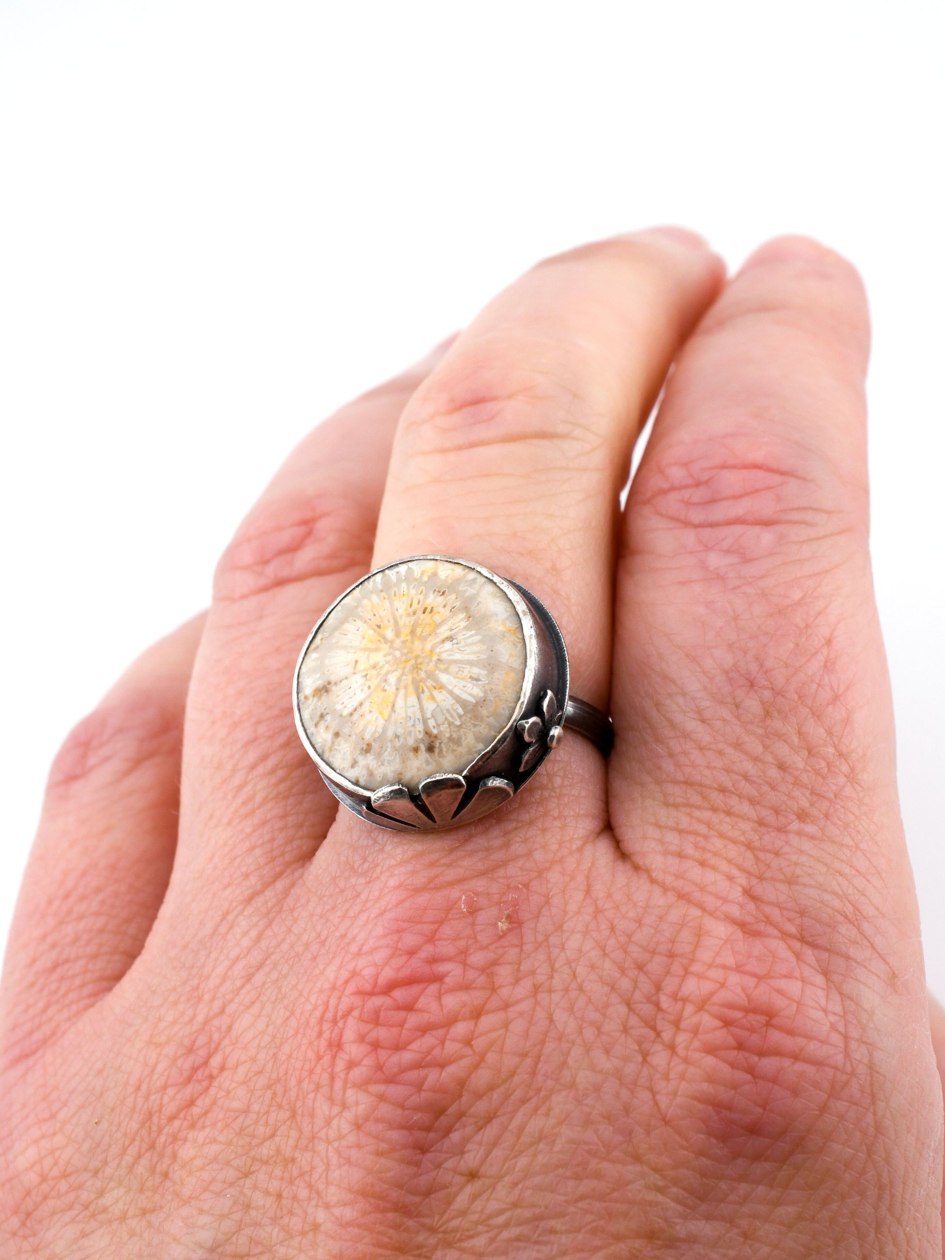 Close-up of a hand wearing a ring with a natural stone design on a white background