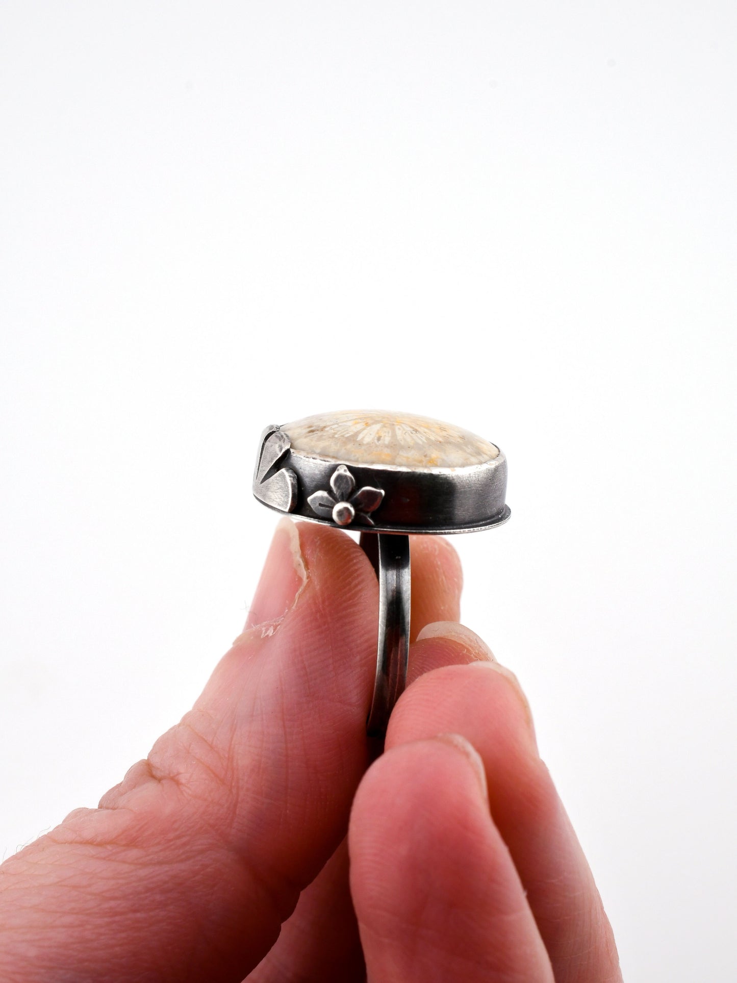 Silver ring with a floral design held between fingers against a white background