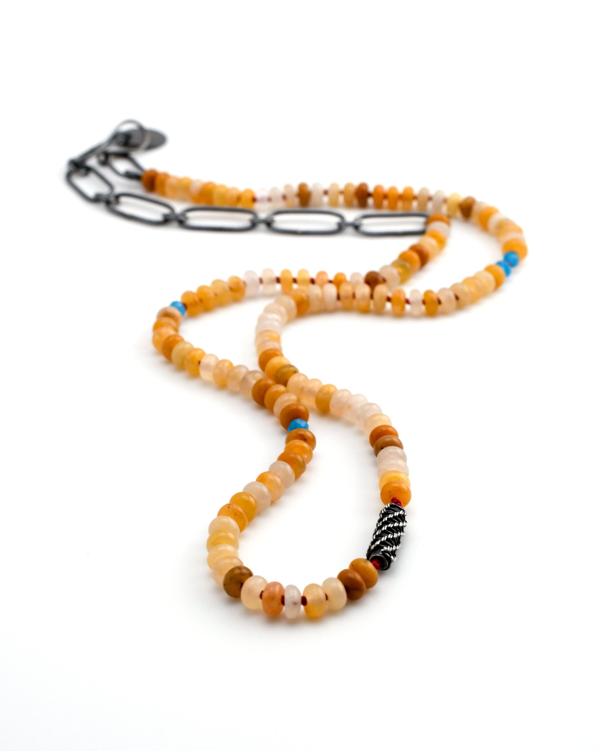 yellow jade beaded necklace with blue apatite accents and a silver woven bead and black silver chain on a white background