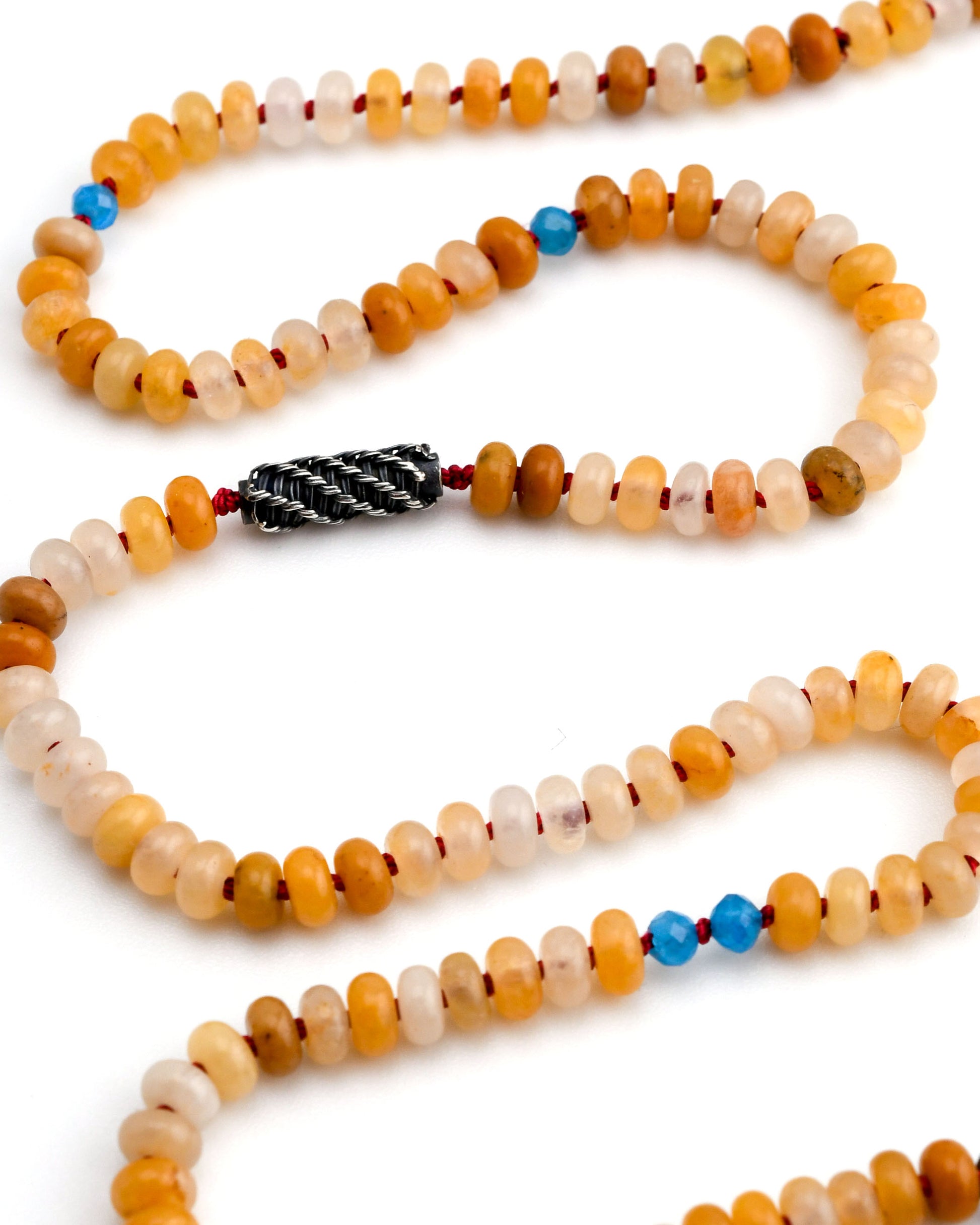detail of yellow jade beaded necklac with blue apatite accents and a woven silver bead on a white background