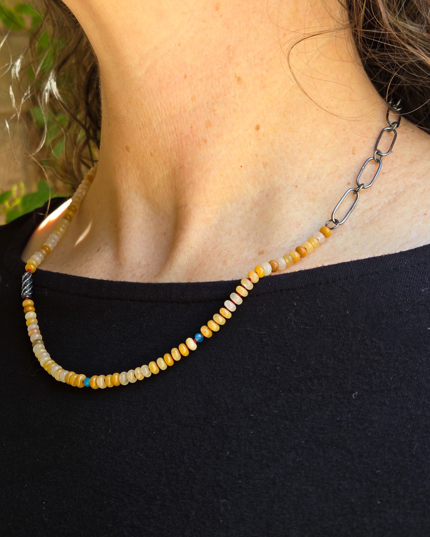 Necklace with yellow beads and a chain on a person wearing a black top.