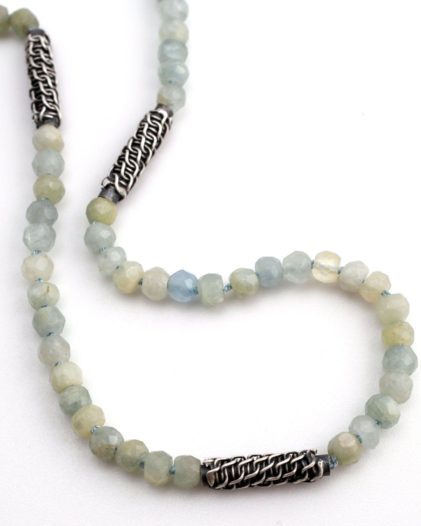 detail of aquamarine beaded necklace on knotted blue silk with woven silver bead accents on a white background