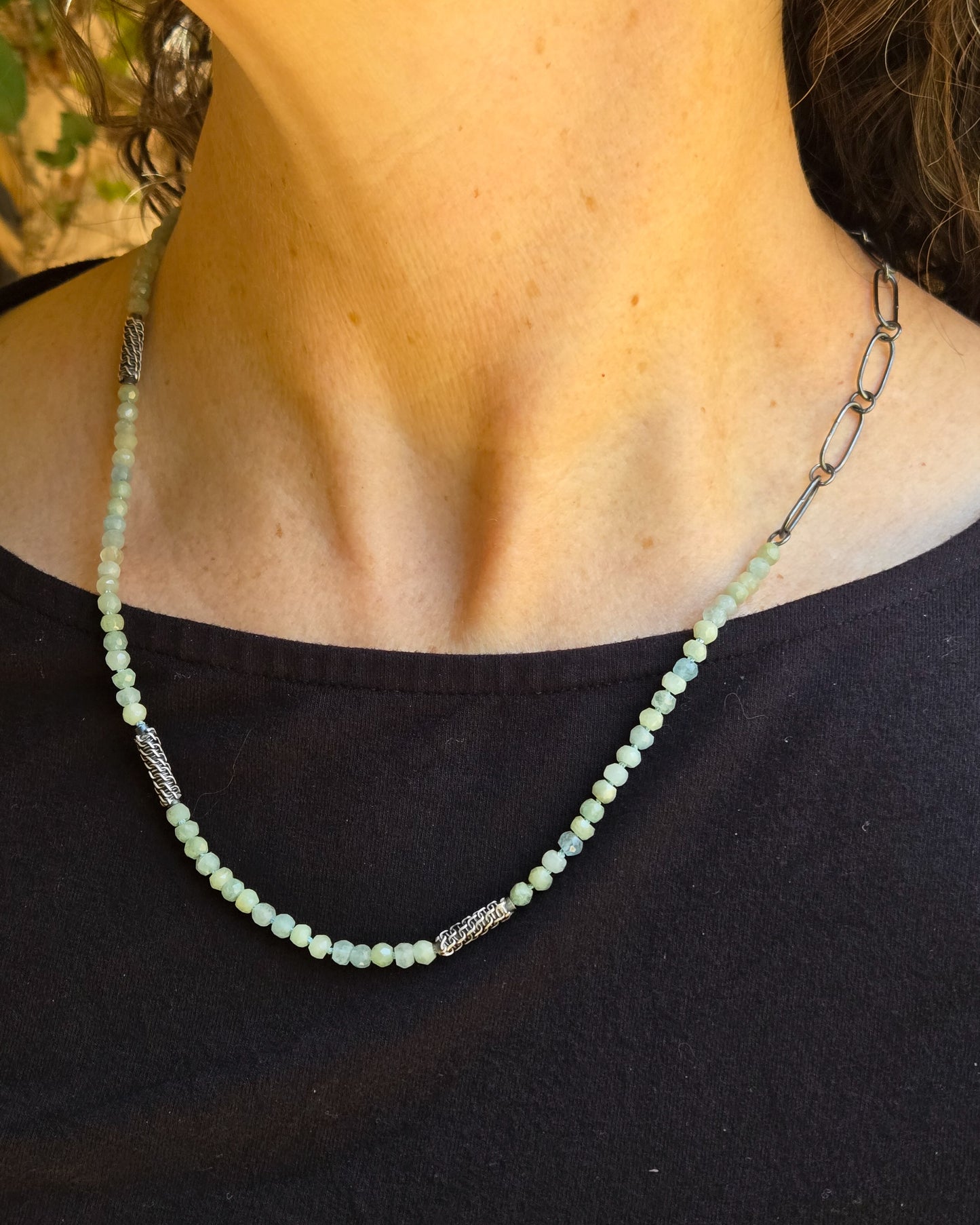 Necklace with blue beads and silver chain on a person wearing a black top.