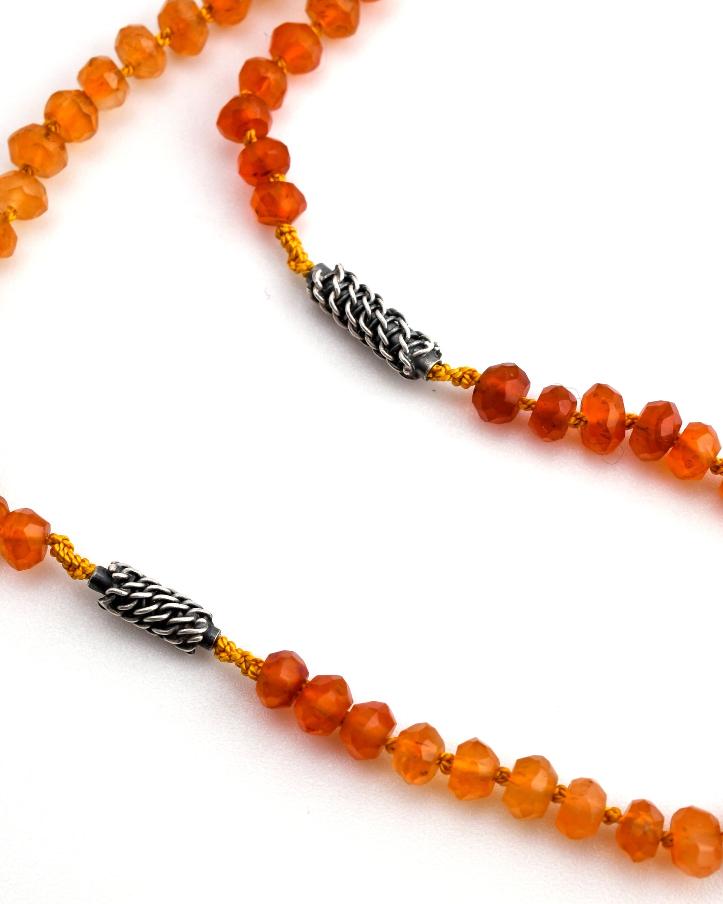 closeup of orange carnelian beaded necklace on yellow knotted silk with woven silver bead accents on a white background