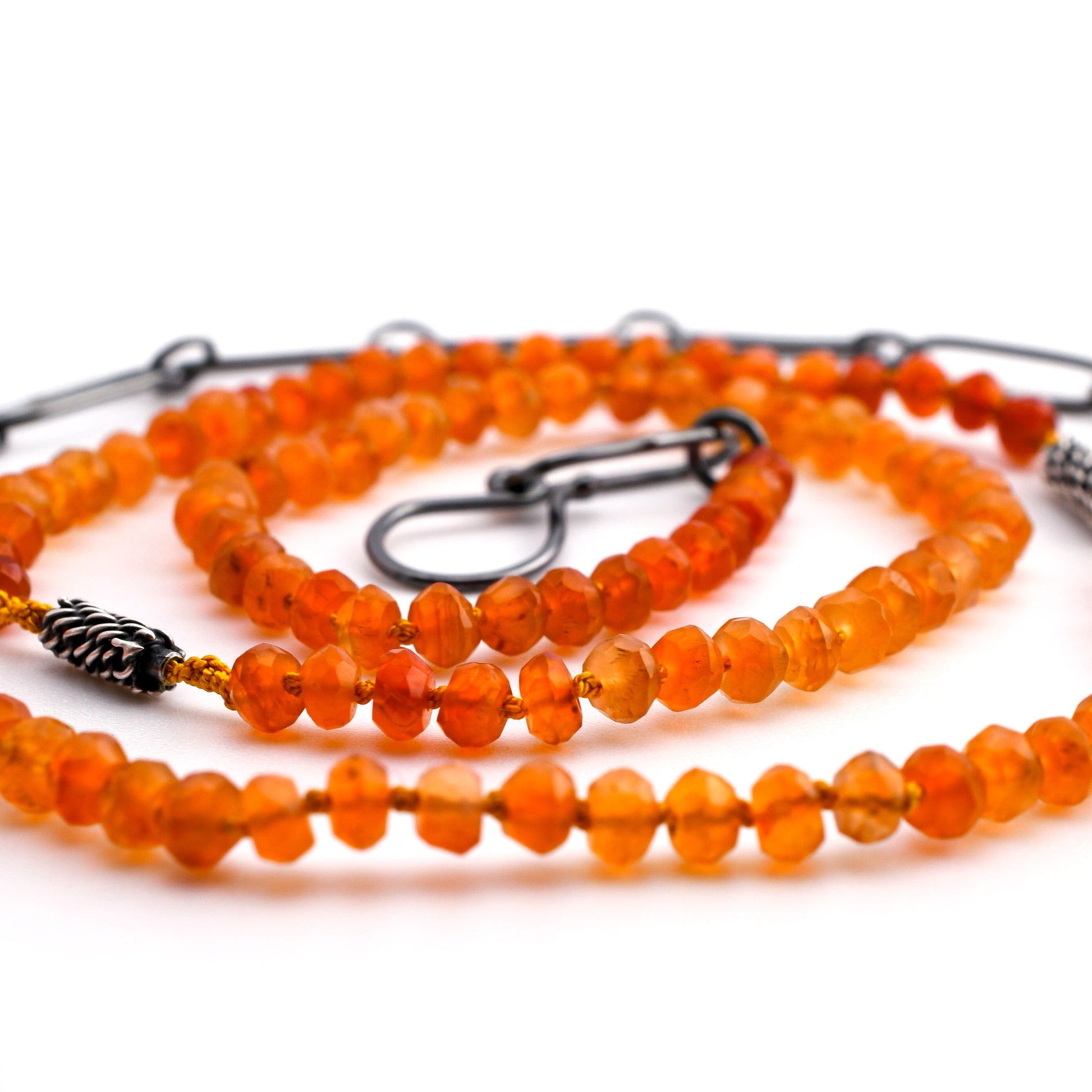 orange carnelian beaded necklace with woven silver bead accents and black silver chain extender arranged in a spiral on a white background