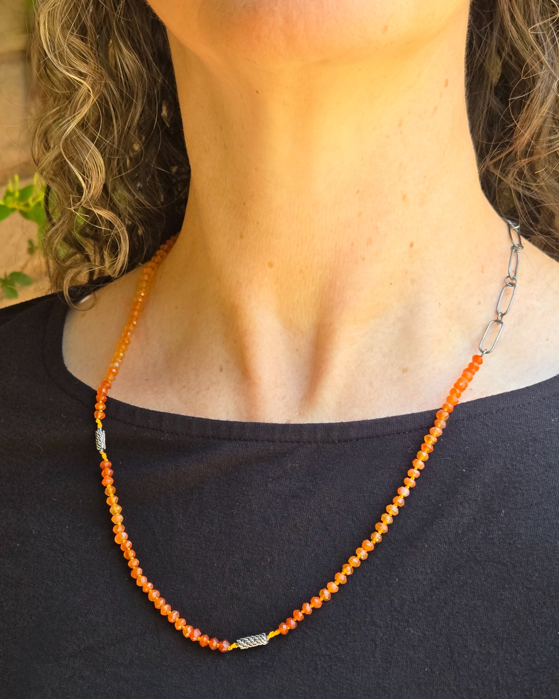 Necklace with orange beads worn by a person against a neutral background