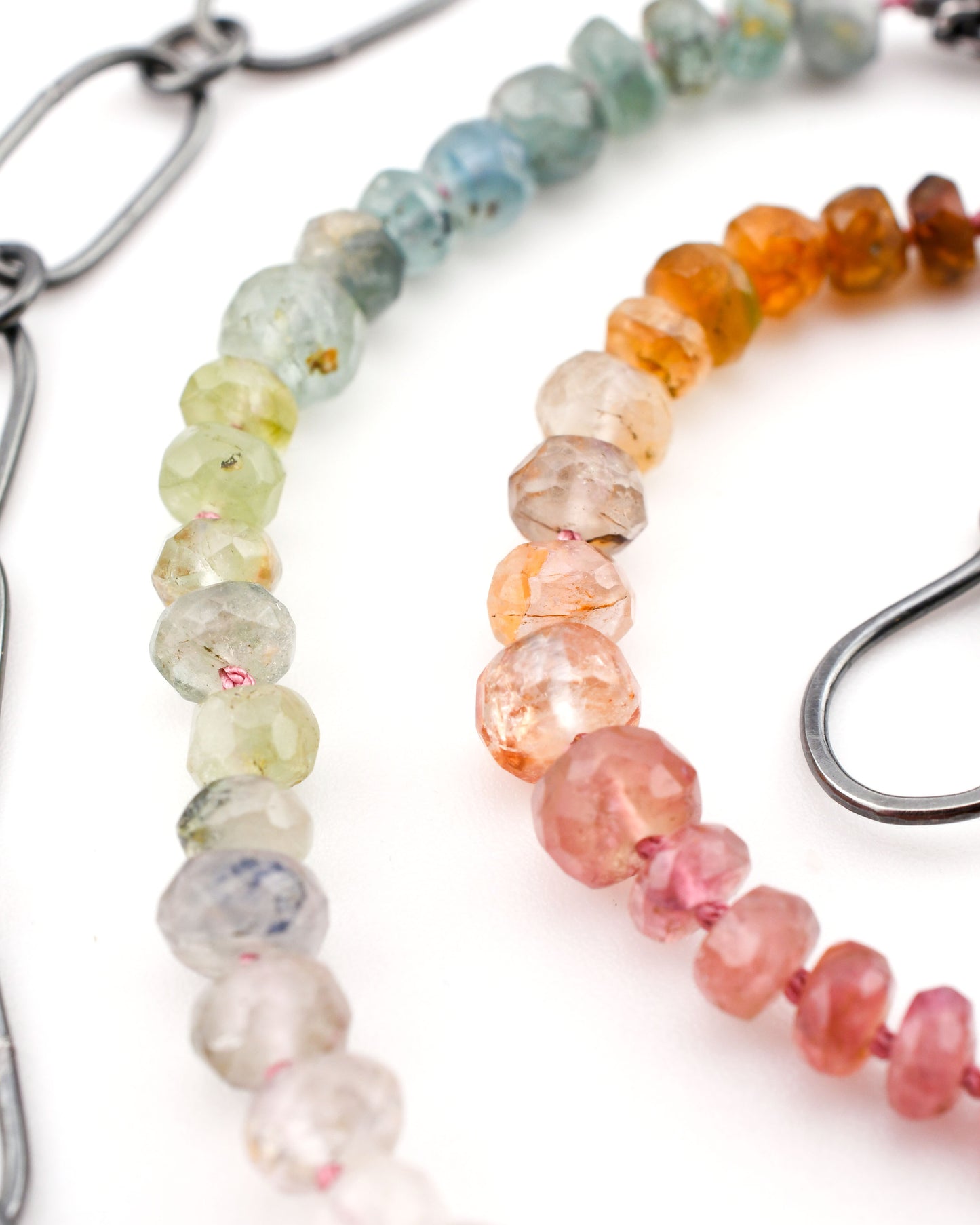 close-up of colorful tourmaline beads and silver chain necklace on a white background