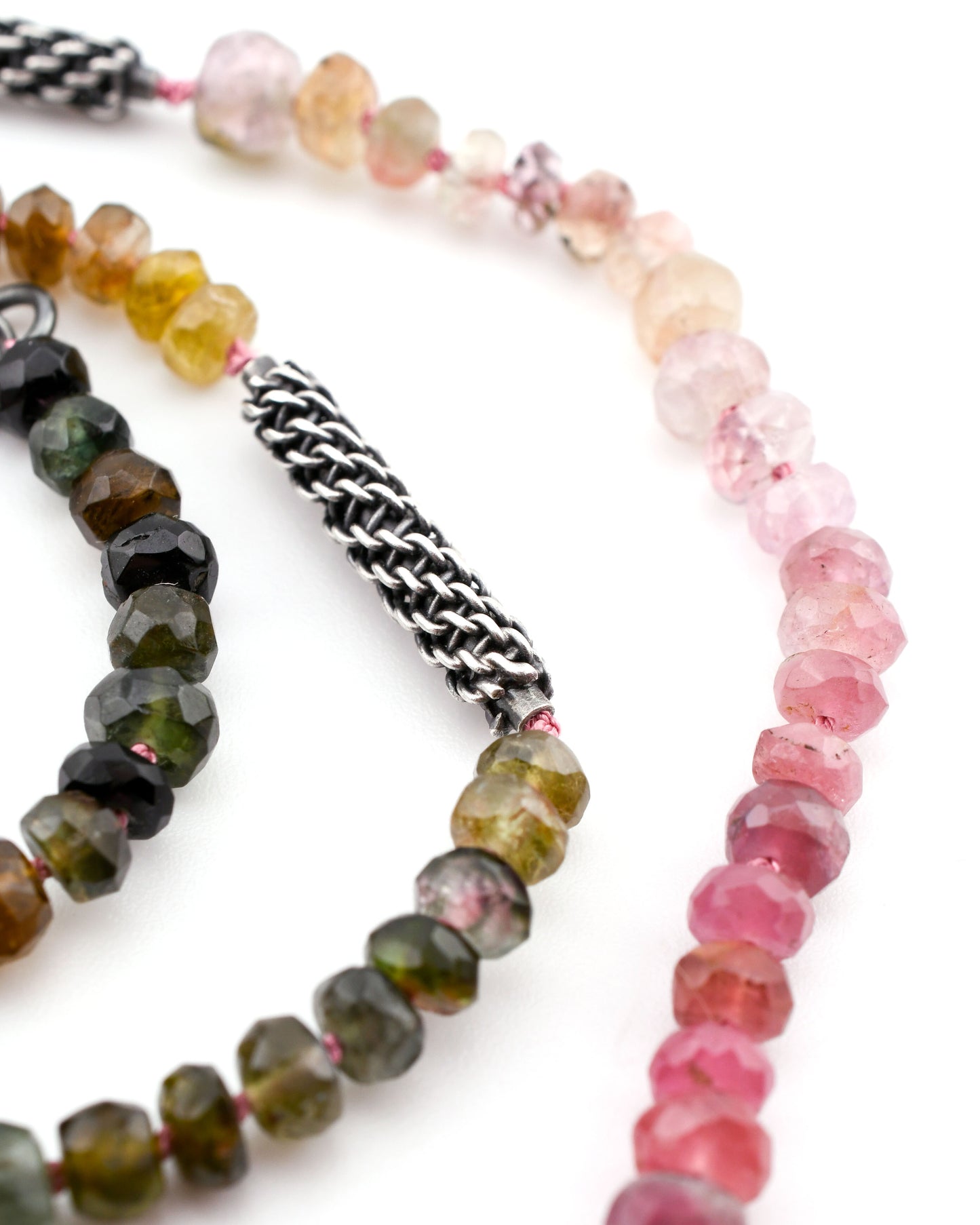 close-up of colorful tourmaline beads and woven silver elements on a white background