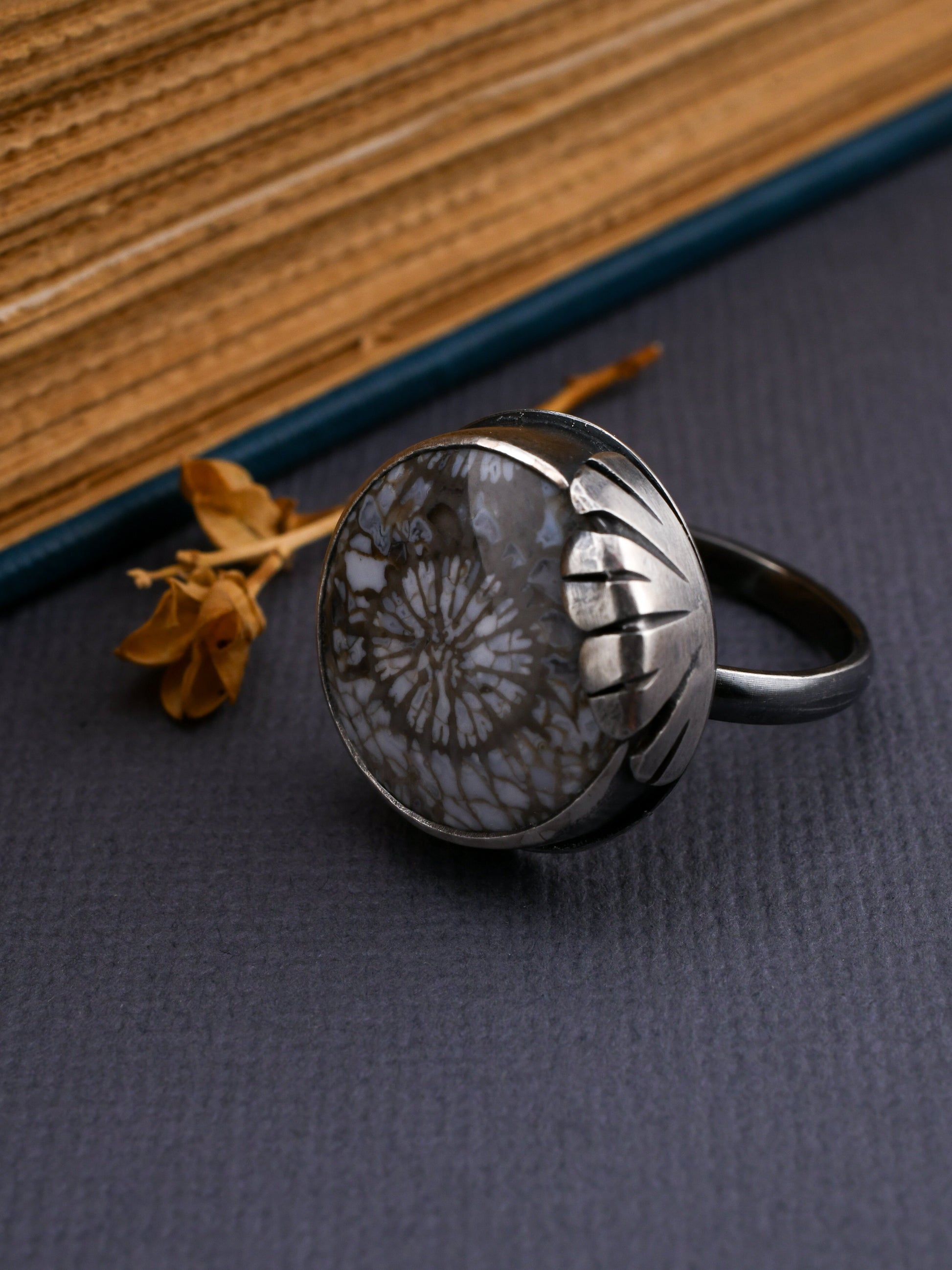 Silver ring with floral design on a dark surface with a book in the background