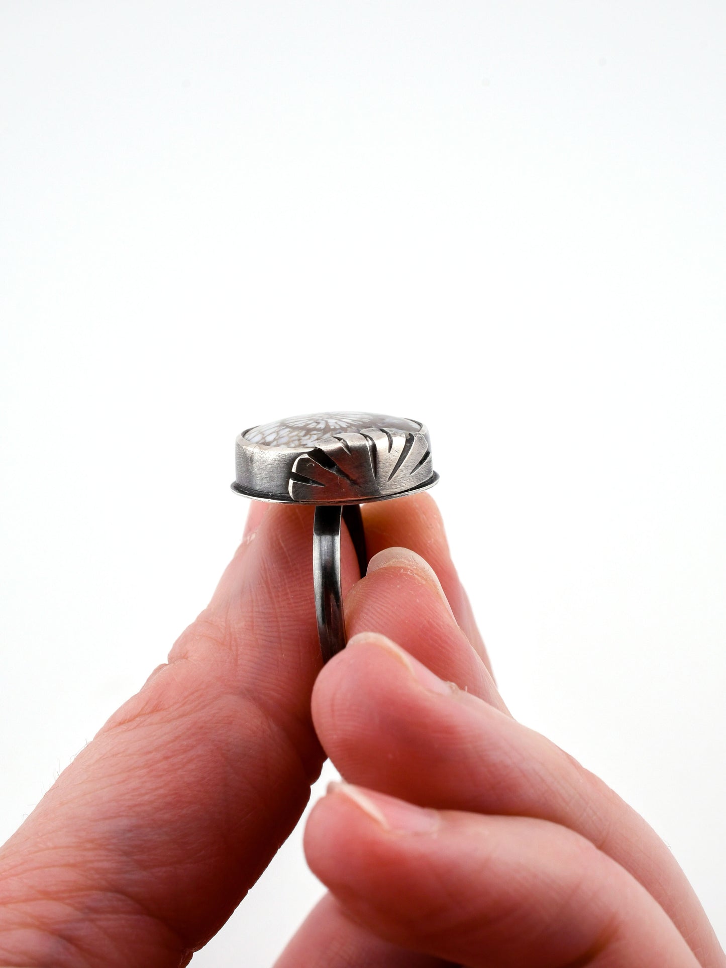 Close-up of a hand holding a silver ring against a white background